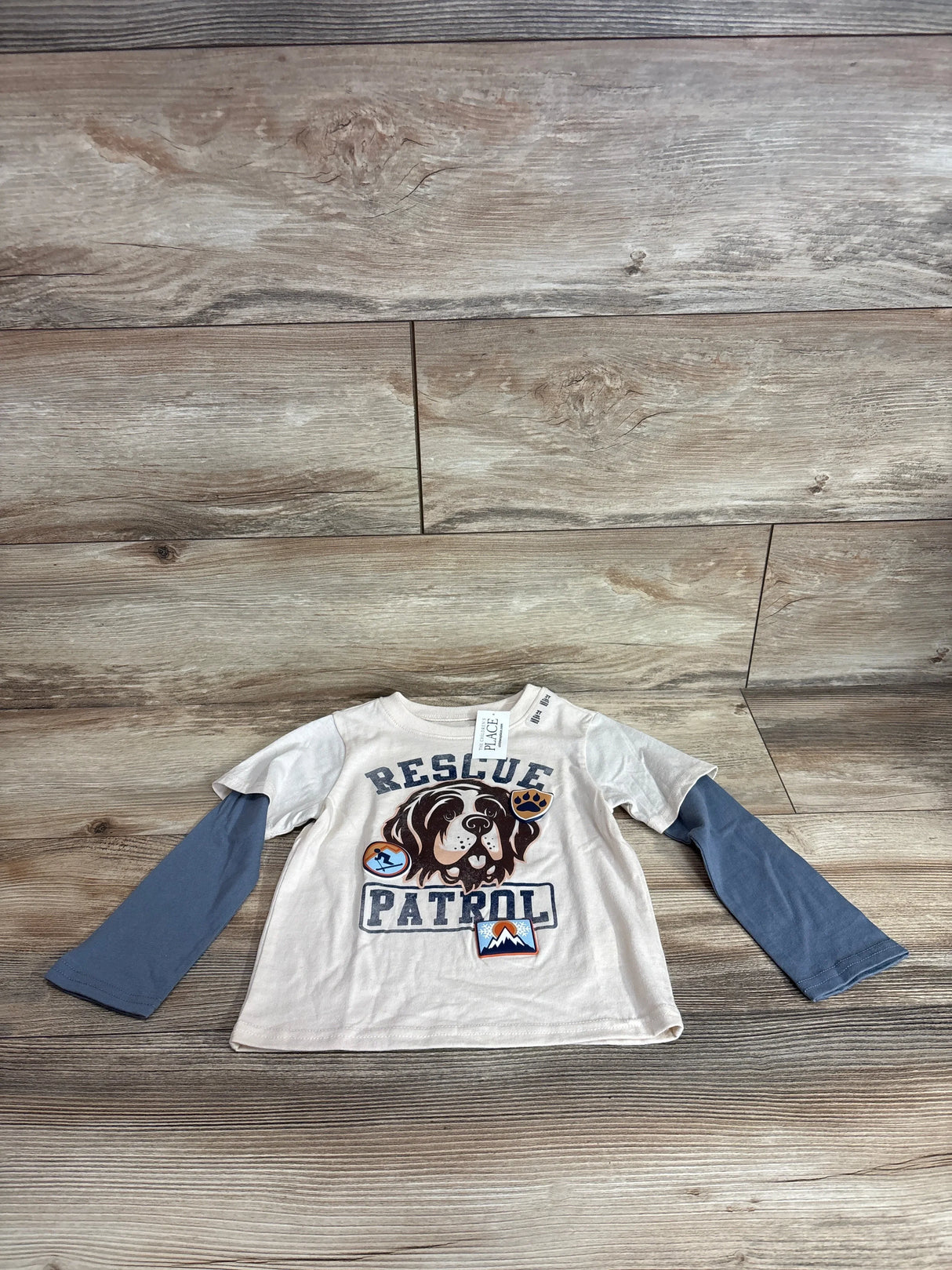 Flat lay of beige toddler long-sleeve shirt with Rescue Patrol text and dog graphic and blue layered sleeves on wood background