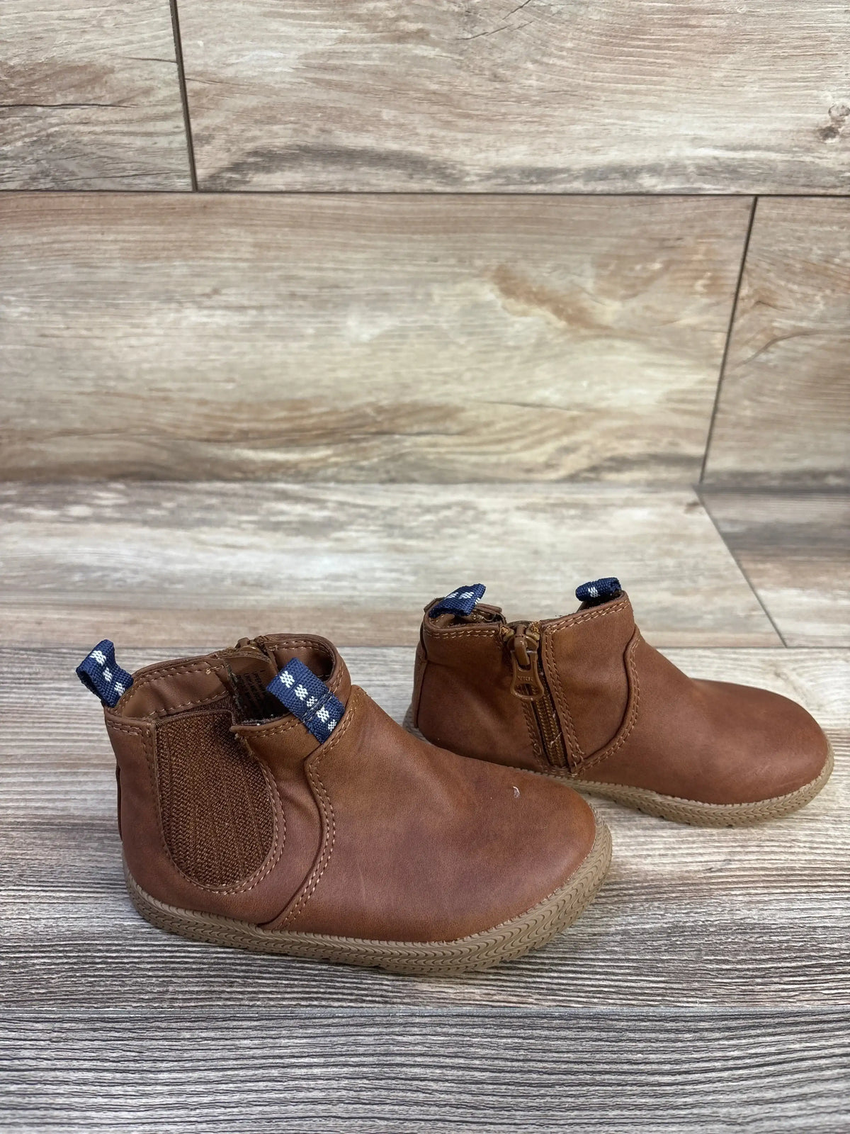 Side view of Cat and Jack Esteban toddler brown zipper boots showing elastic side panel, inner zipper and blue pull tabs on wood background