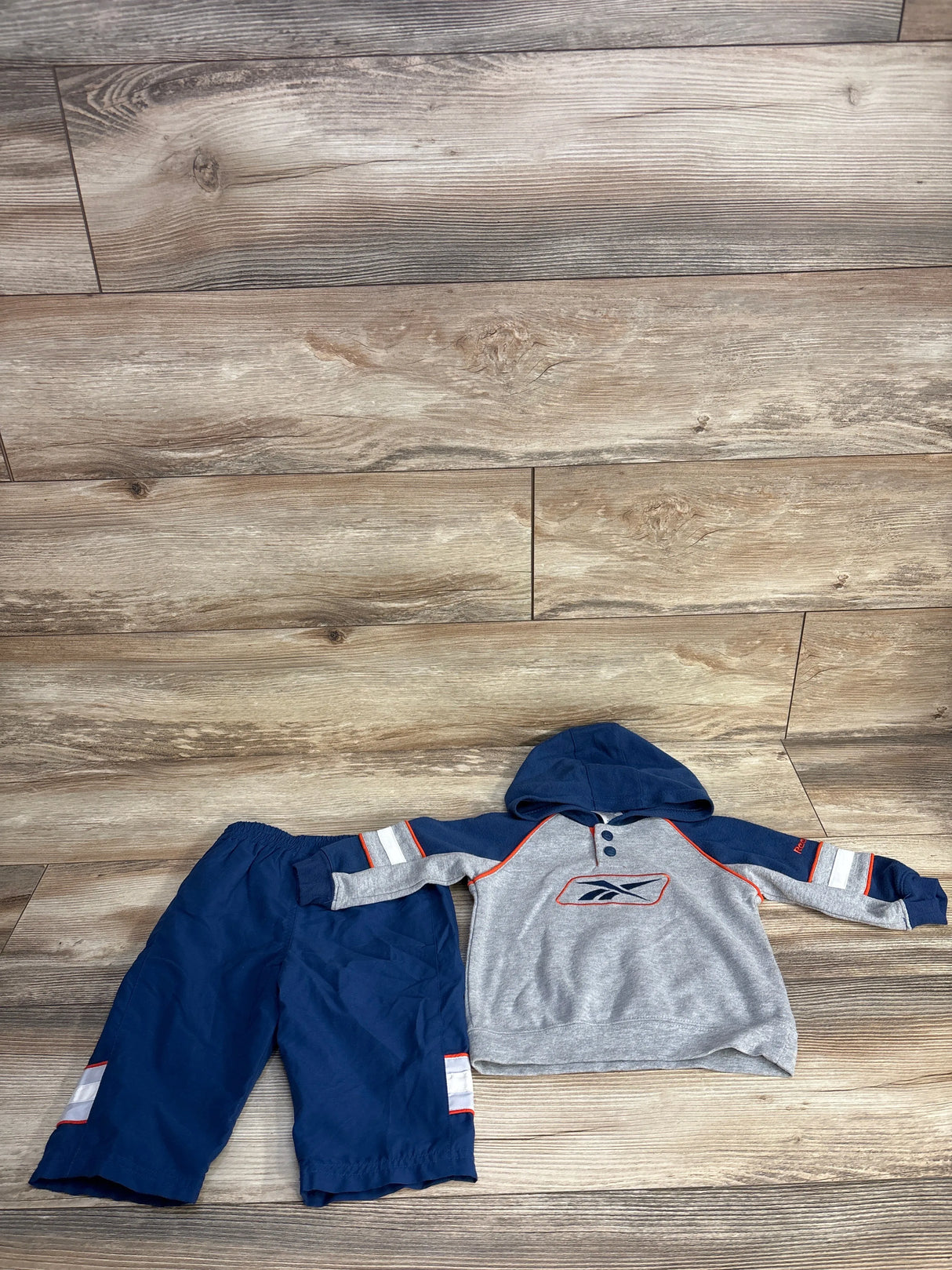Children's navy blue and gray hoodie with matching navy pants featuring red and white accents on wooden floor
