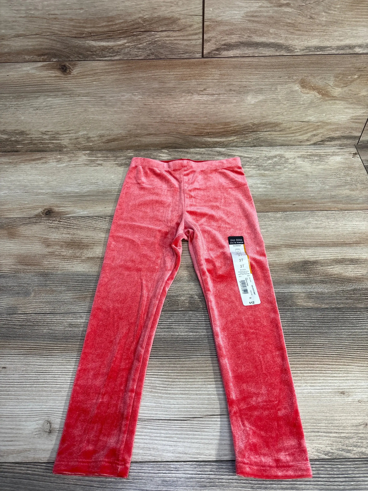 Flat lay of Okie Dokie crushed velvet toddler leggings in red, size 3T, showing attached size tag on wood floor background