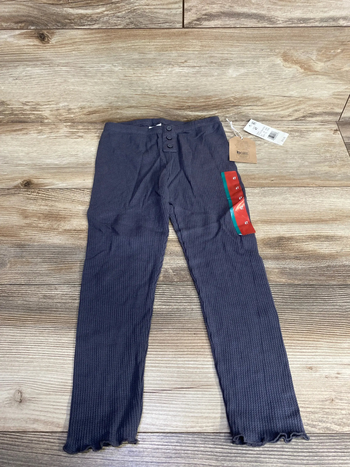 Girls’ dark ribbed knit pants with button detail and tags, laid on wood floor