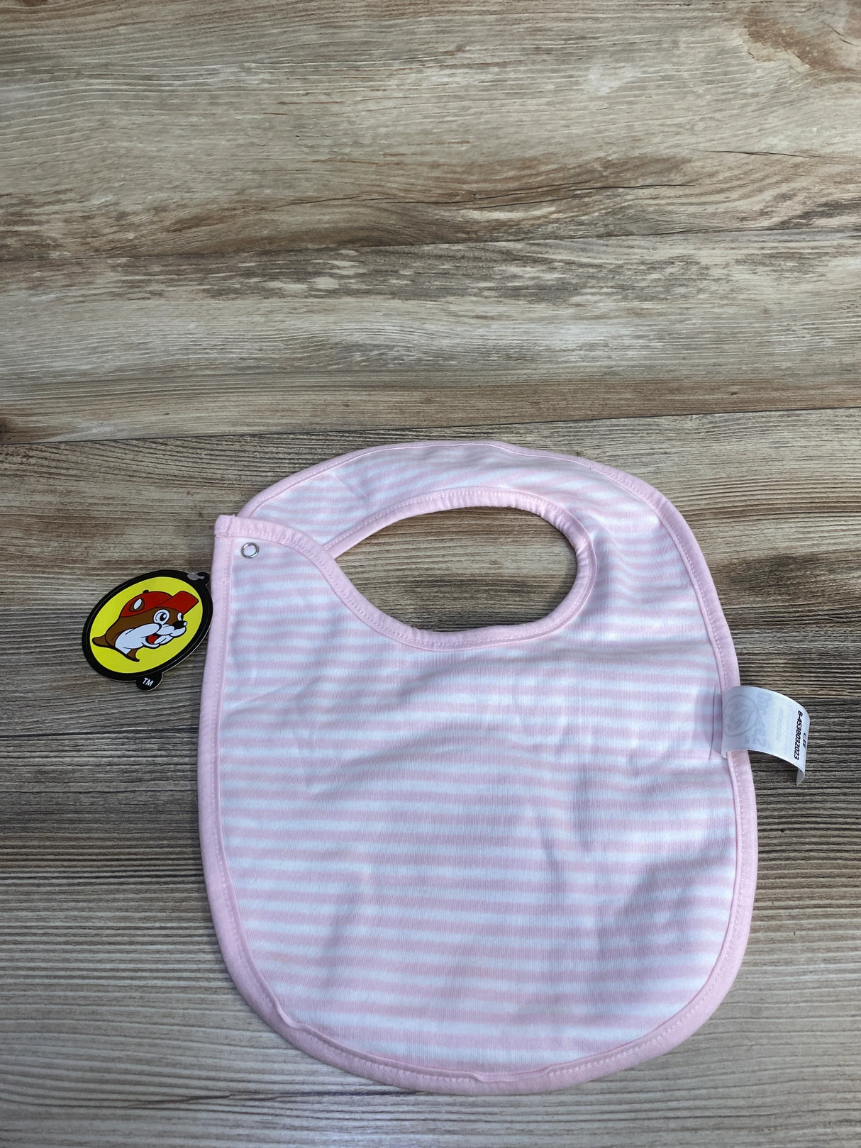 Pink and white striped baby bib with round neck opening on wooden surface