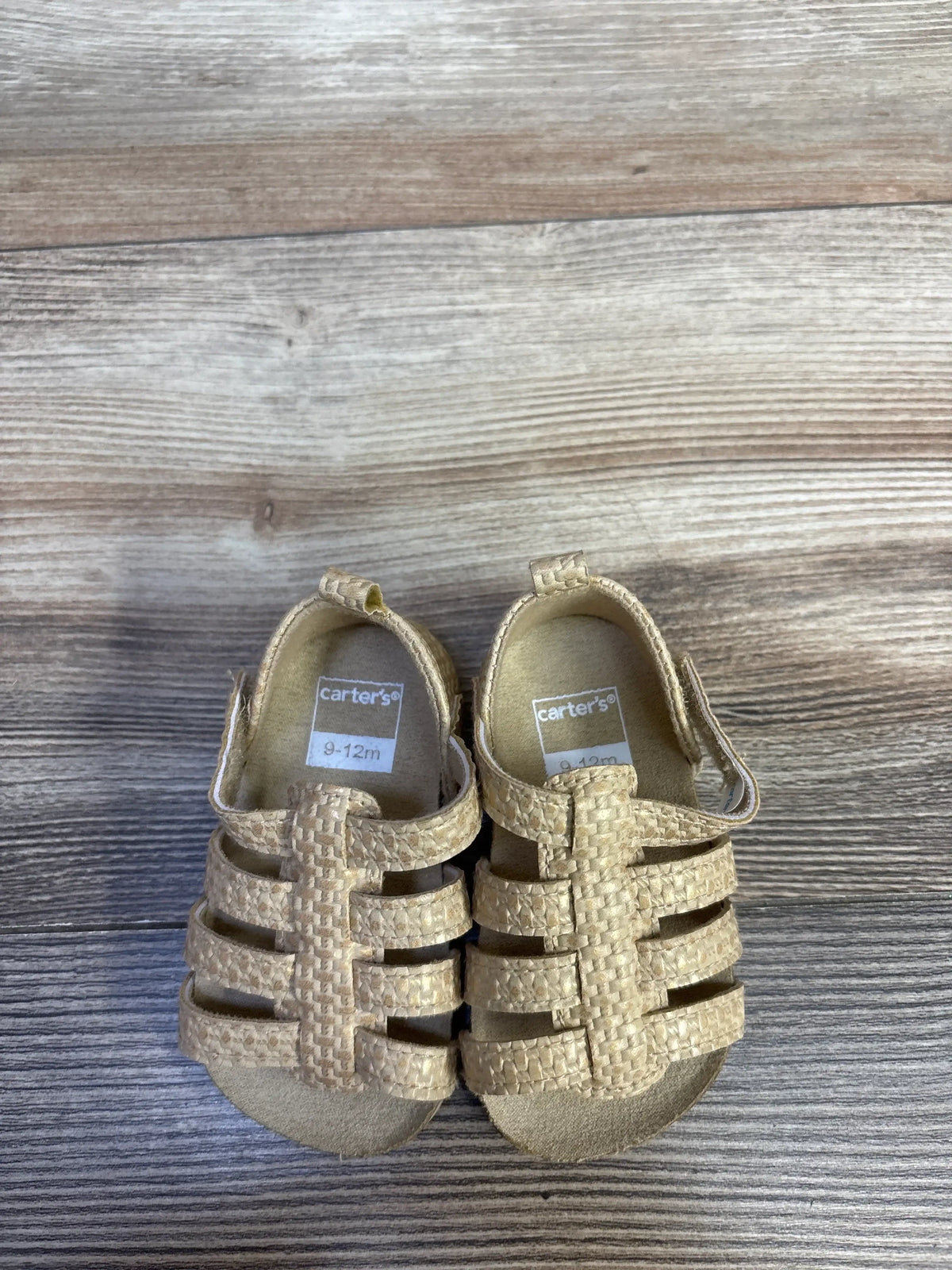Top view of Carter’s strappy sandals showcasing solid brown woven straps and open toes on a wood-grain background