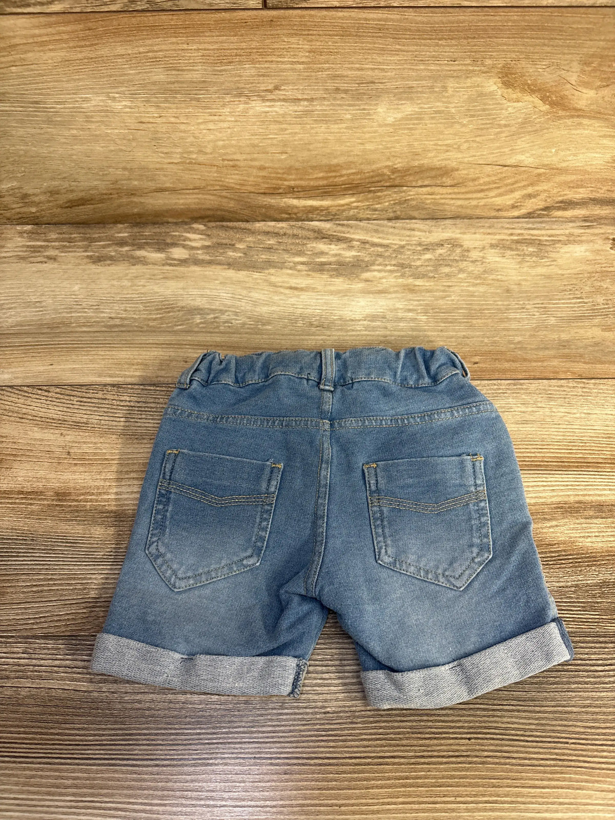 Back view of Fox denim drawstring shorts showcasing rolled cuffs and two back pockets on a wood surface