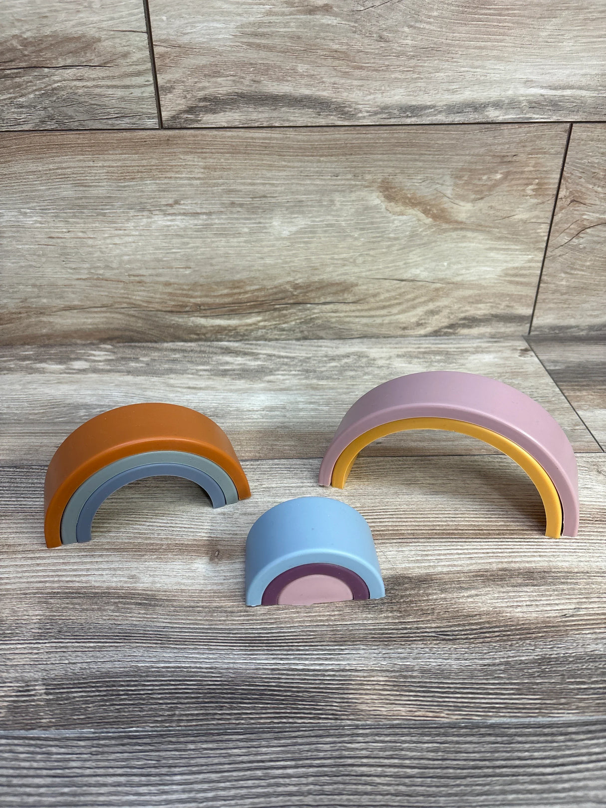 Front view of Twinkle Twinkle Little One silicone rainbow stacker with three separated dusty pastel arches on wood surface