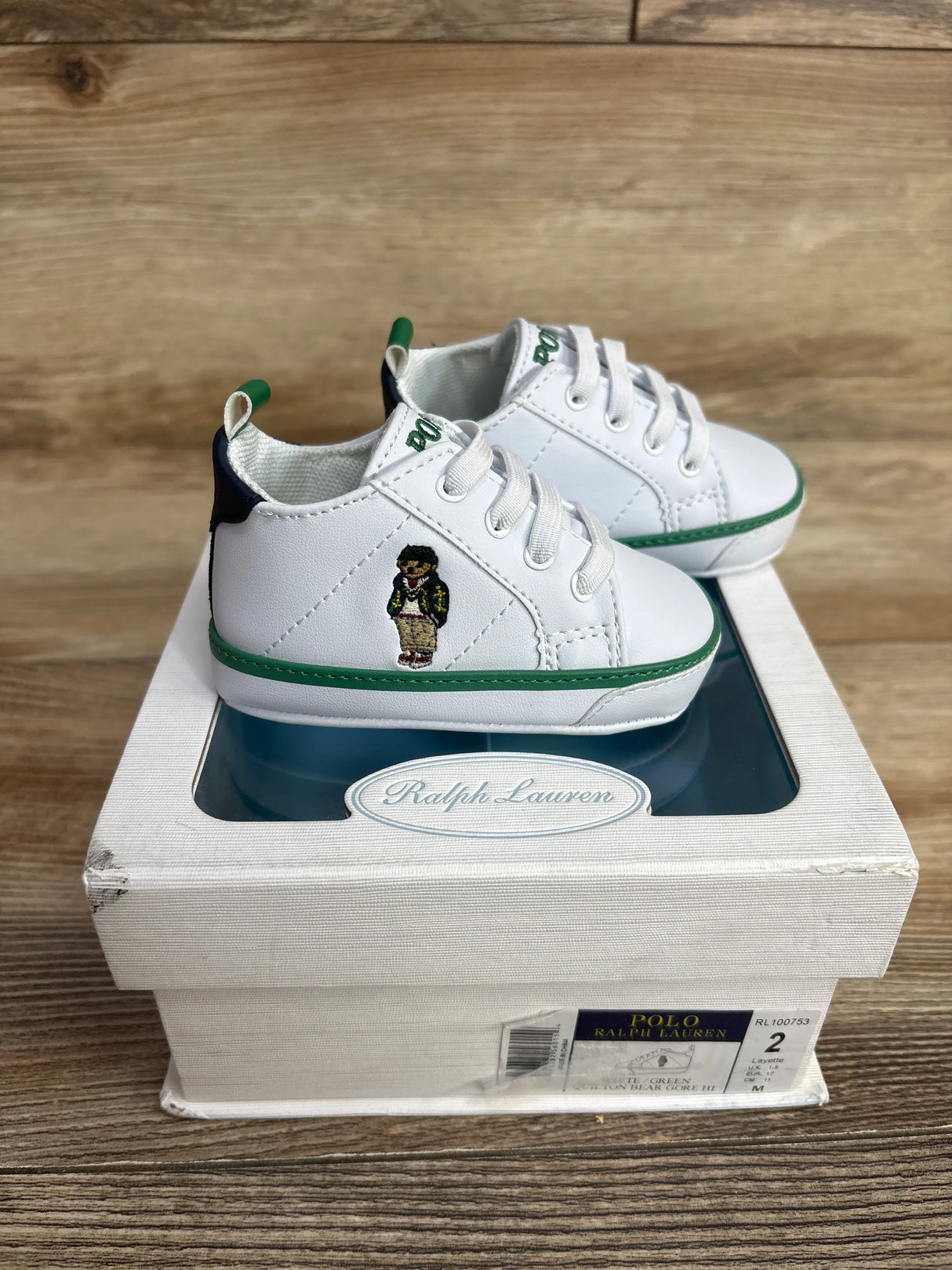 White Polo Ralph Lauren baby sneakers with green trim and bear embroidery on top of white shoe box