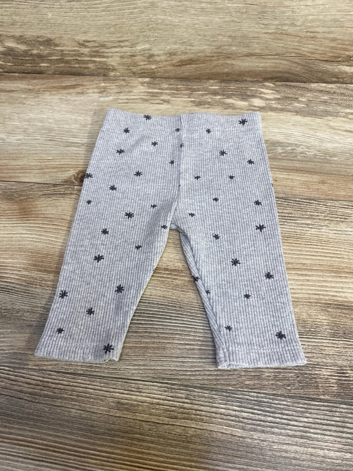 Front view of grey ribbed baby leggings (3-6 months) showcasing ribbed texture and small dark star print on wood background