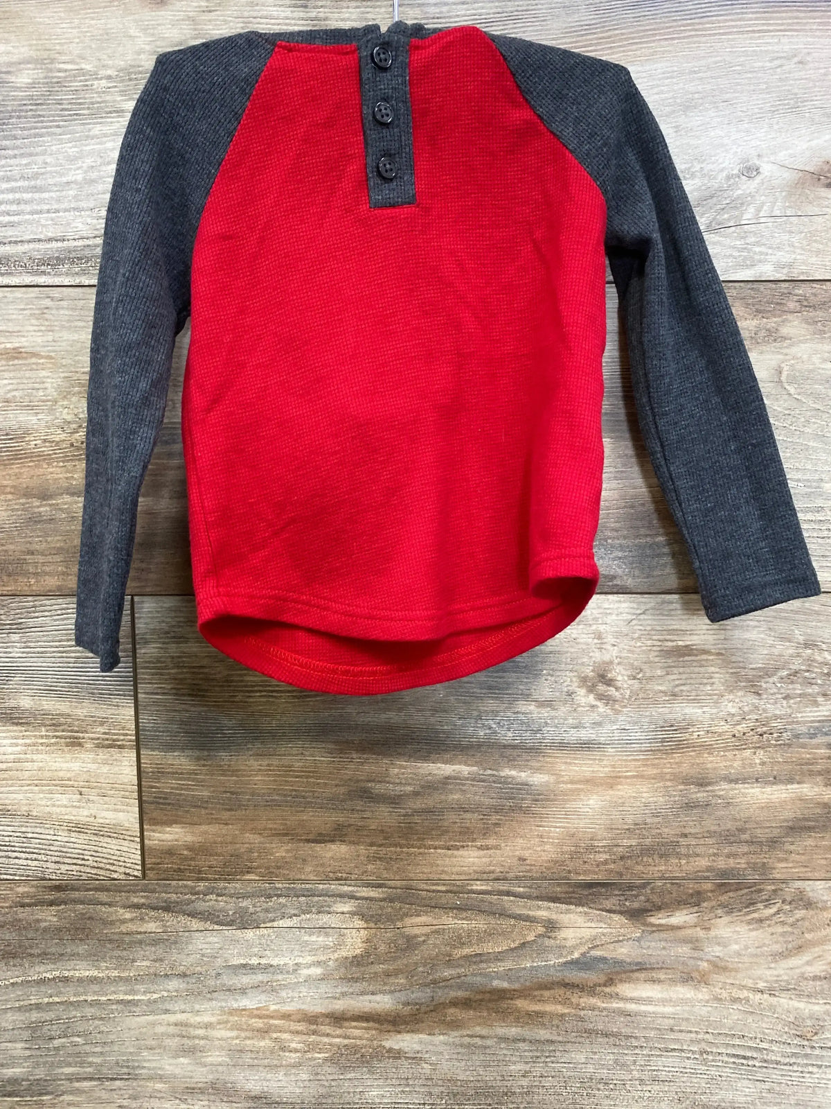 Long sleeve kids henley shirt with red body and dark gray sleeves on wood background