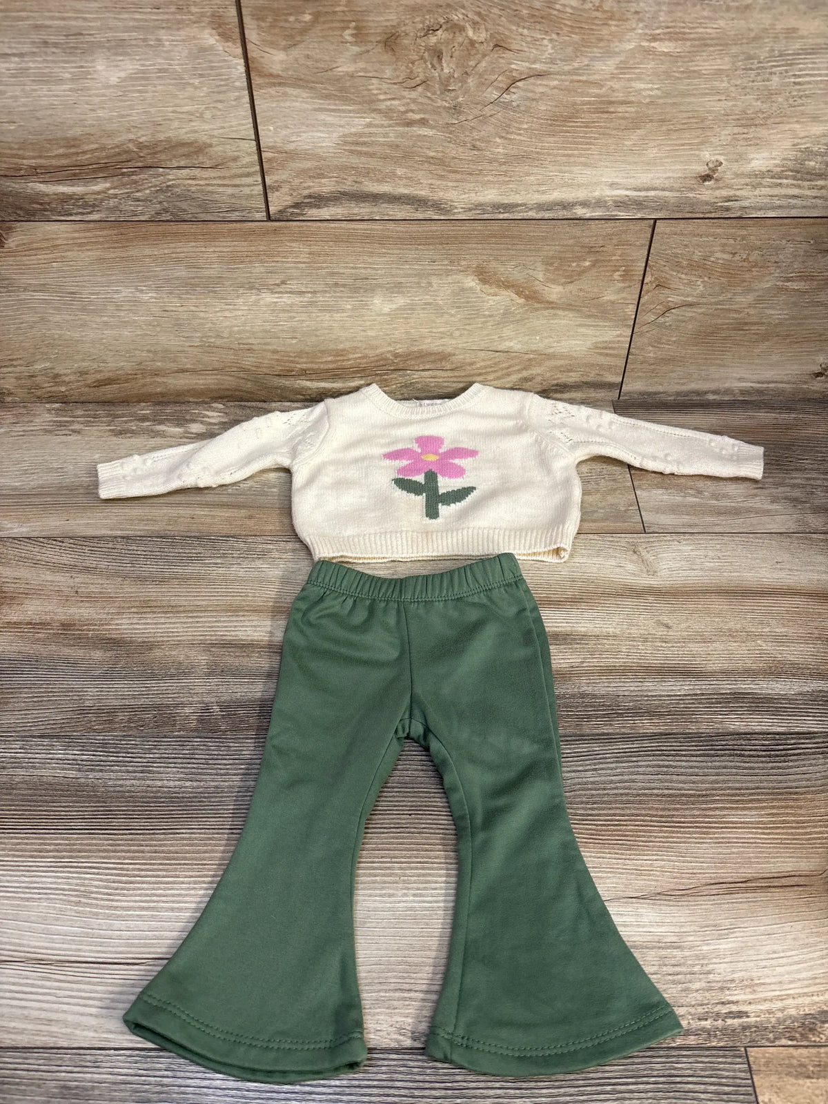 Front view of Btween baby knit sweater and flare leggings set with flower graphic and dark green flared leggings on wood floor