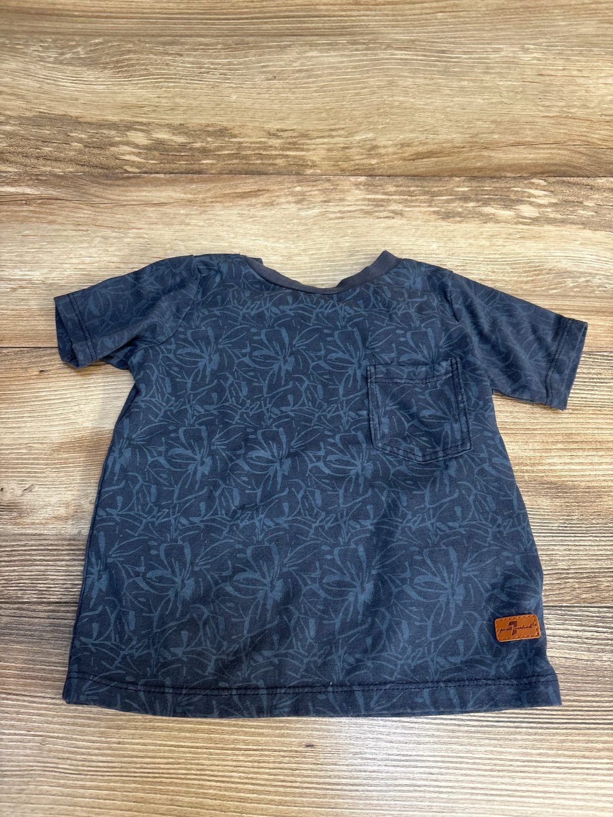 Blue floral print kids t-shirt with chest pocket, laid on wood floor
