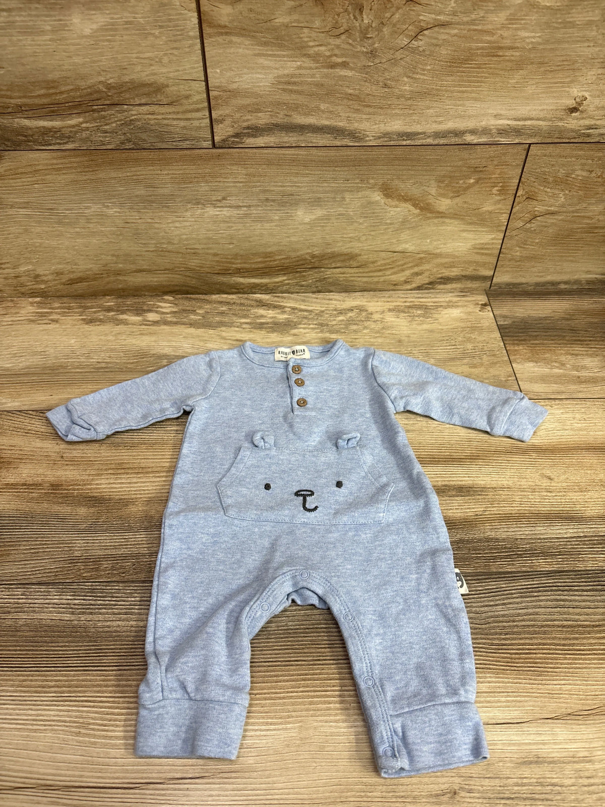 Front view of blue Rabbit + Bear Henley Coverall showcasing long sleeves, three-button placket, bear-face pocket, and snap closures