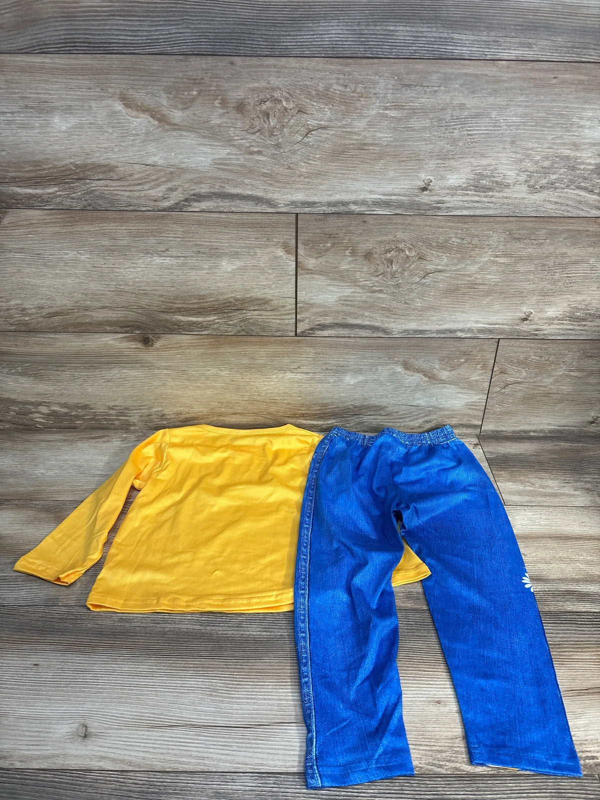 Flat lay showing back of yellow long-sleeve toddler shirt and blue elastic-waist pants on wood floor