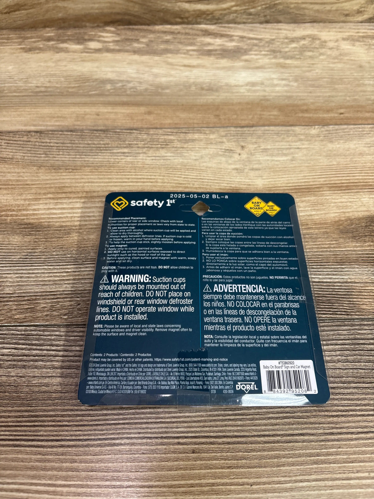 Back view of Safety 1st Baby On Board sign and car magnet pack with bilingual warnings on wood-grain background