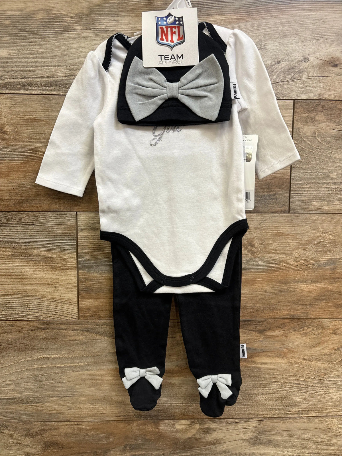 Front view of Raiders baby 3-piece set: white bodysuit with black trim, black footed pants with gray bows and matching hat