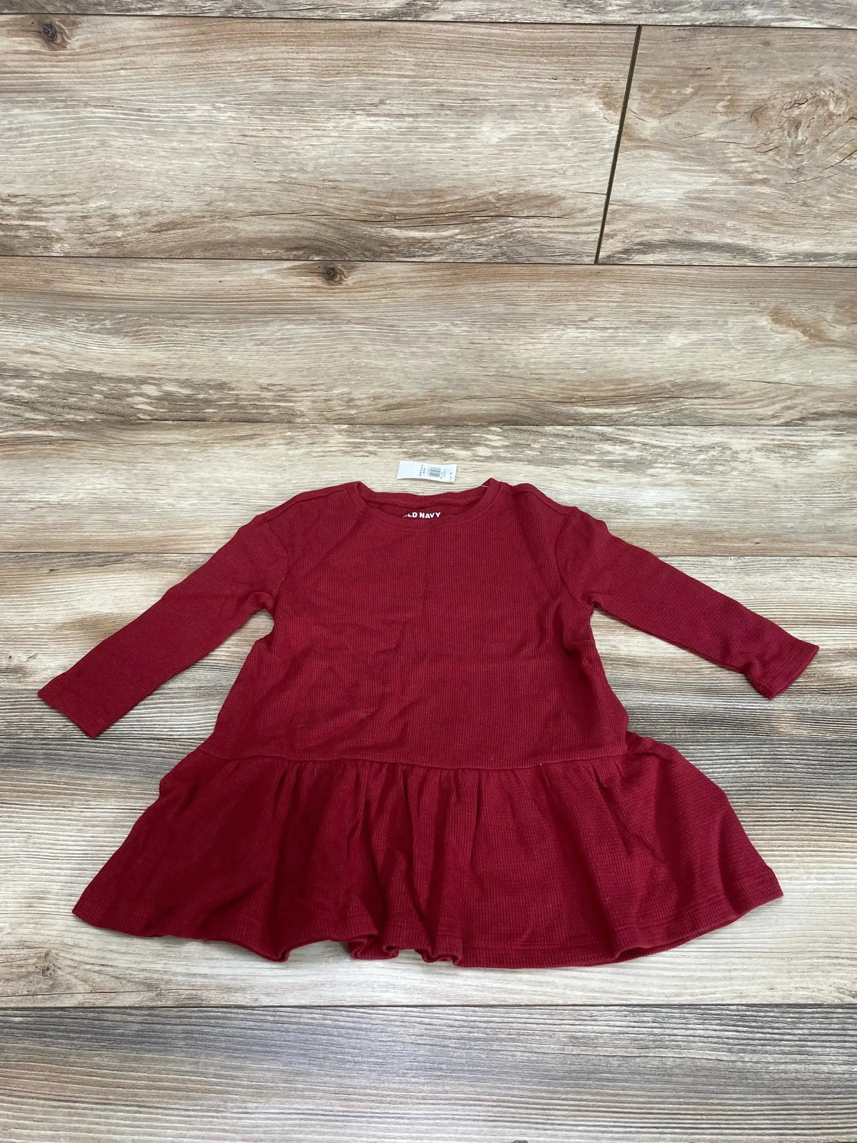 Flat lay of Old Navy peplum thermal dress in crimson, size 18-24 months showcasing ruffled peplum hem and waffle knit texture on wood floor