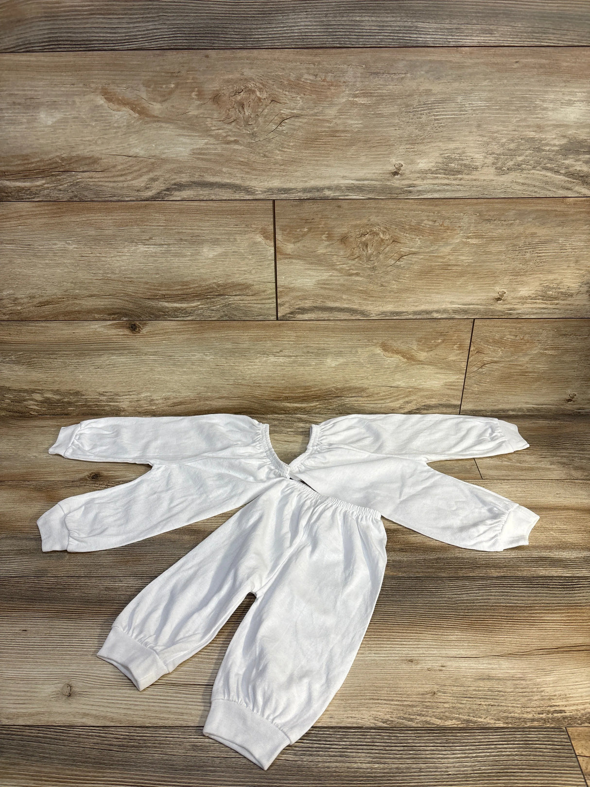 White baby onesie with long sleeves and elastic cuffs on wood floor, ideal for newborns and infants