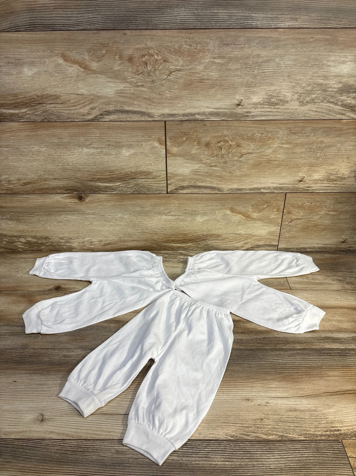White baby onesie with long sleeves and elastic cuffs on wood floor, ideal for newborns and infants