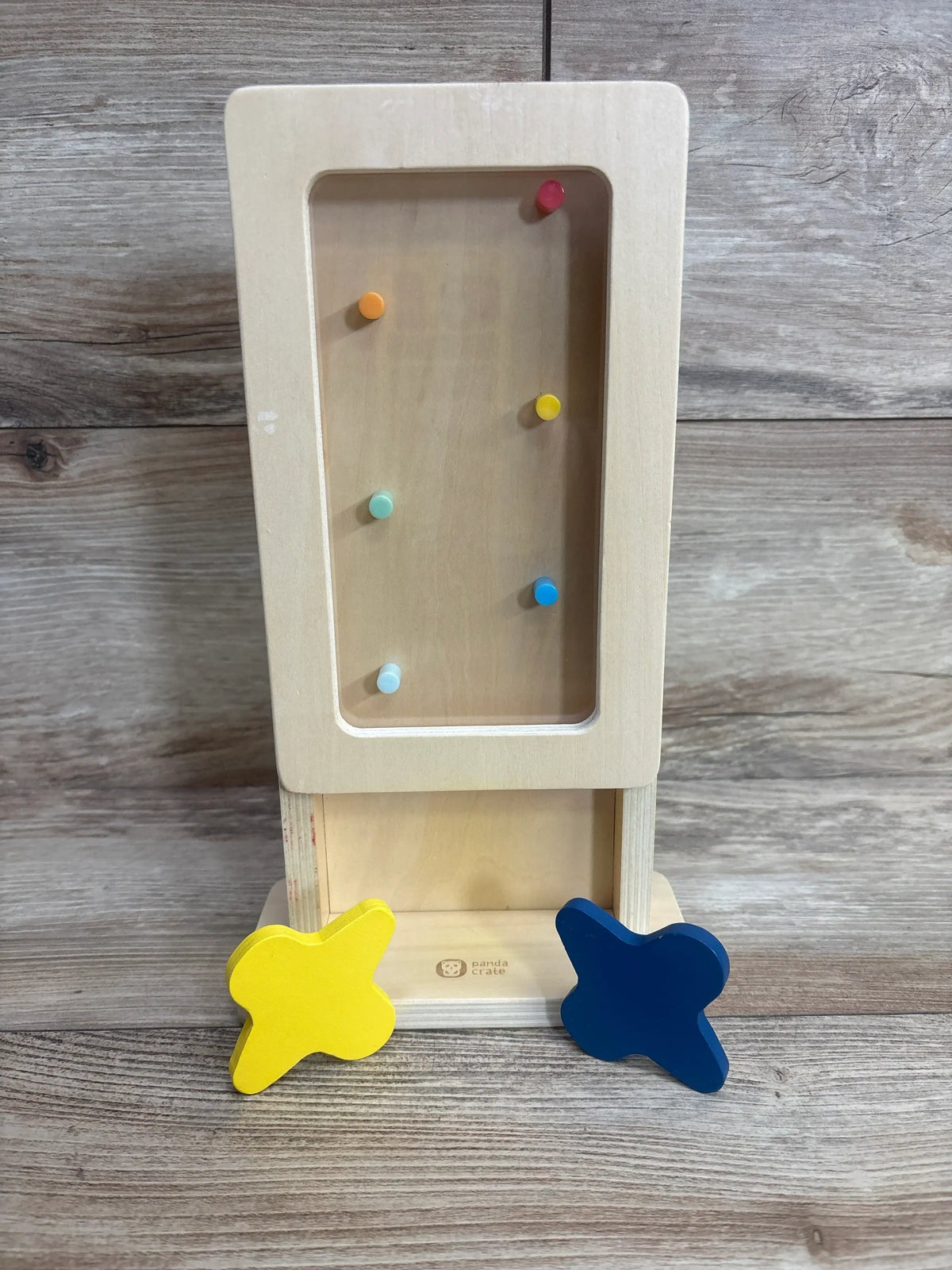 Front view of KiwiCo Star Drop Maze showing six colorful pegs and two wooden star shaped pieces on a wood background