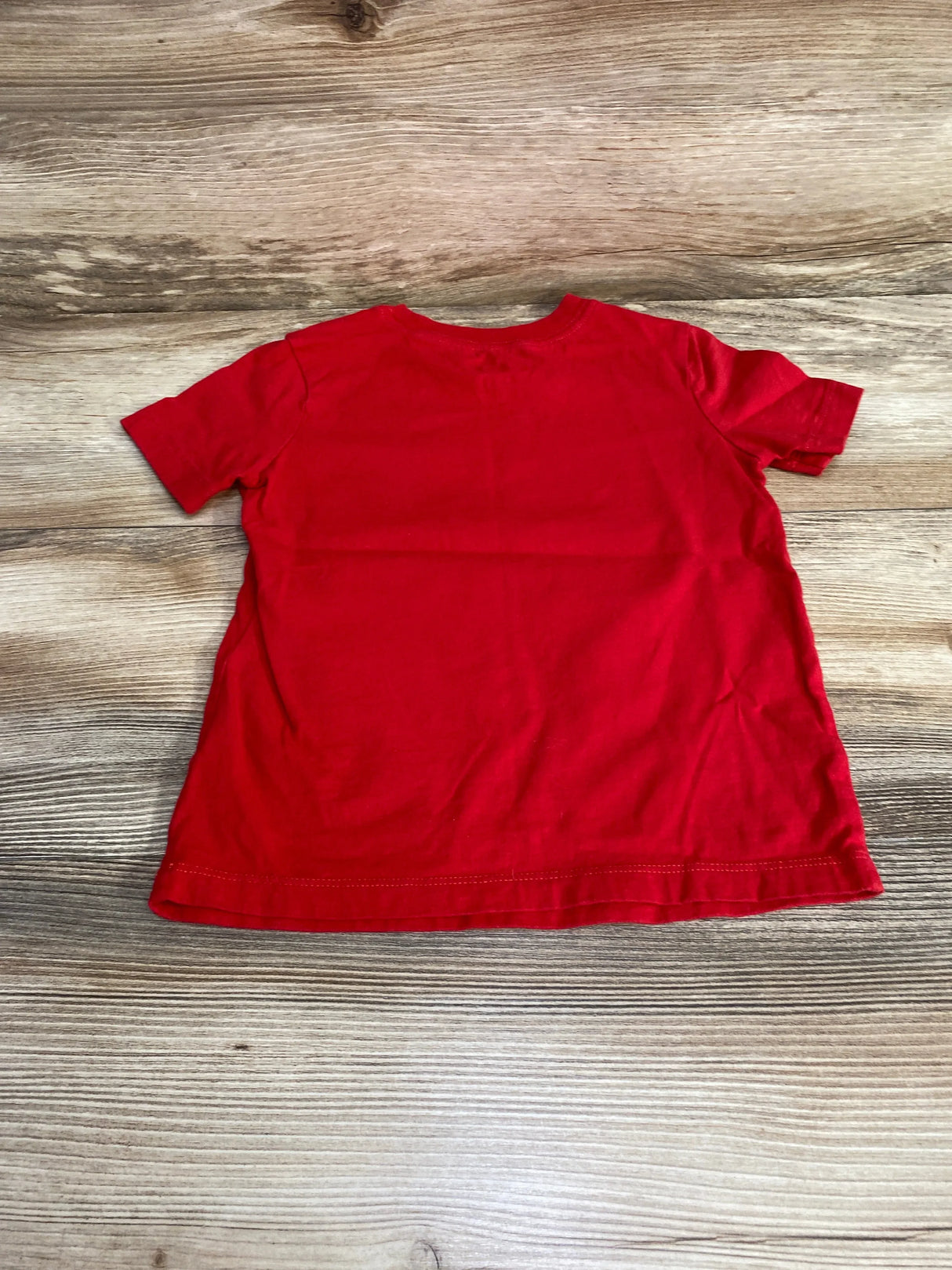 Back view of red OshKosh short-sleeve toddler t-shirt size 3T laid flat on wood background showing plain back with light wrinkles