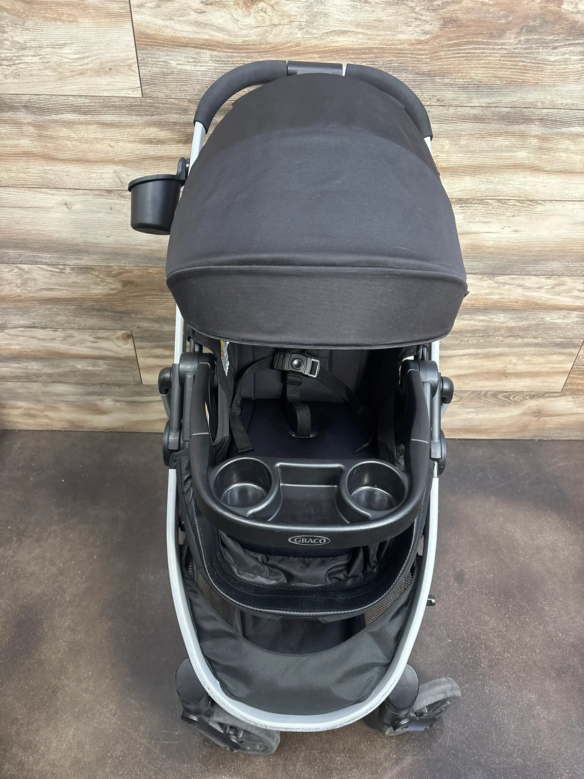 Front view of black Graco Modes Pramette stroller showcasing canopy, five point harness, dual cup holder tray, and storage basket