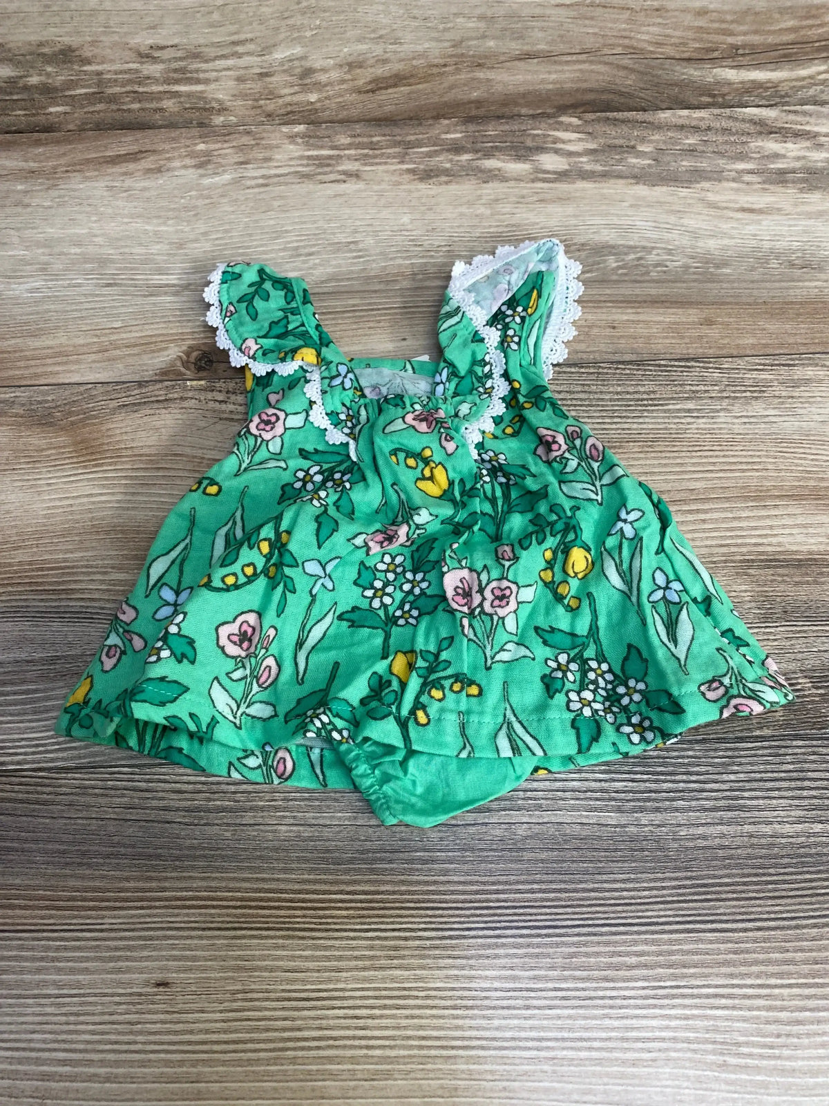 Flat lay of newborn Cat & Jack green floral sleeveless dress with matching bloomers, lace-trimmed straps on wood background