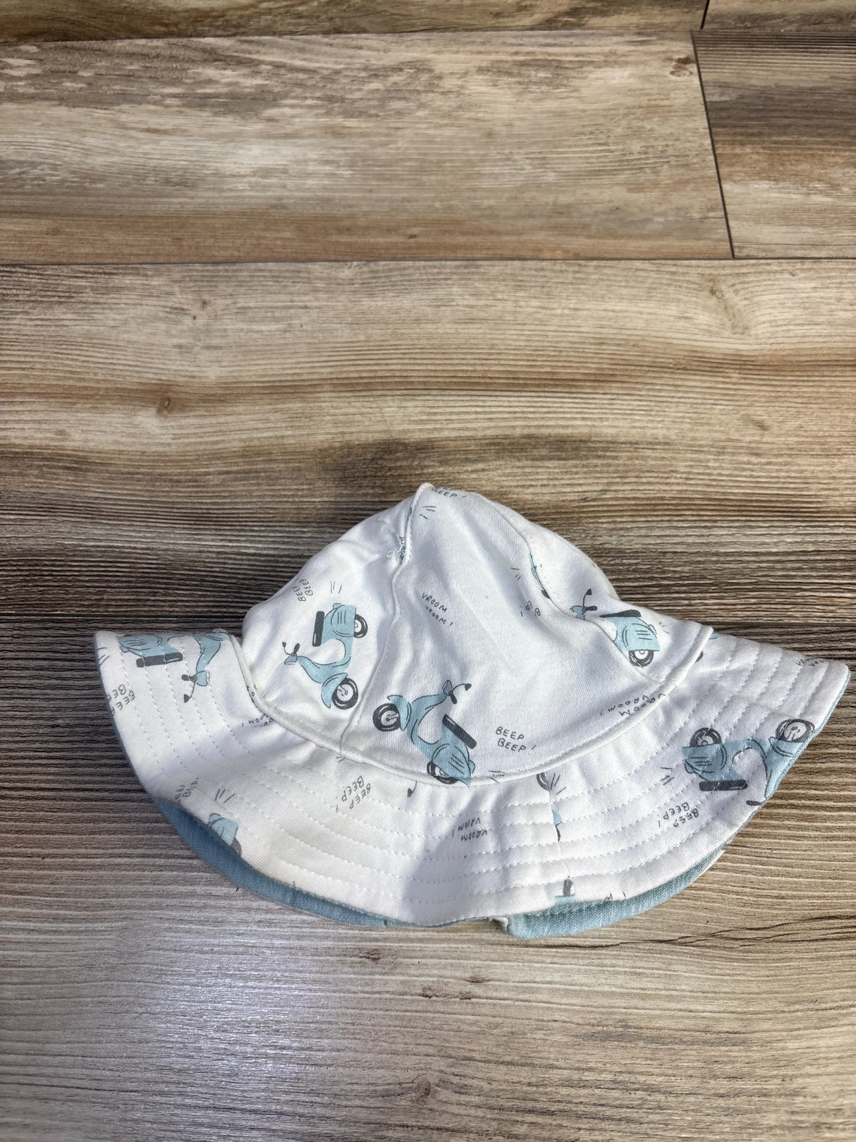 Top view of Carter’s organic reversible baby bucket hat showing white side with blue scooter print and blue reverse on wood