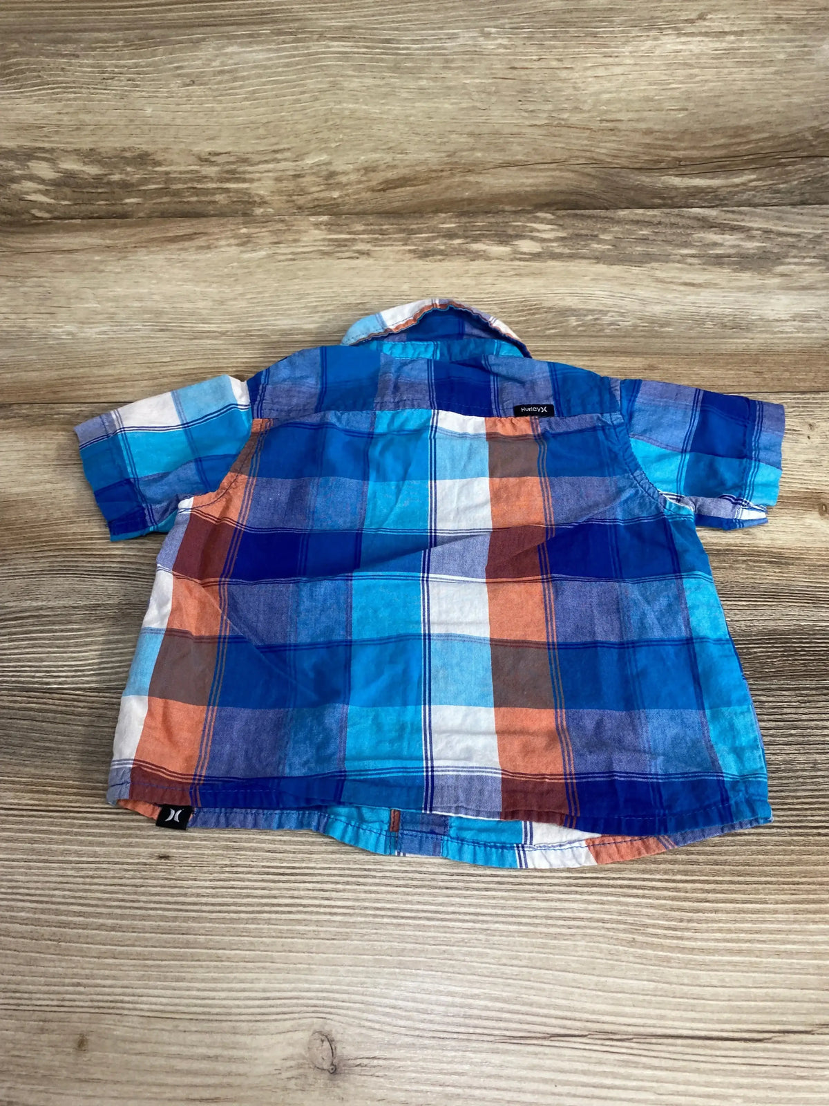 Back view of Hurley plaid short-sleeve button-up shirt 12M showing blue and orange checks and brand tag on wood background