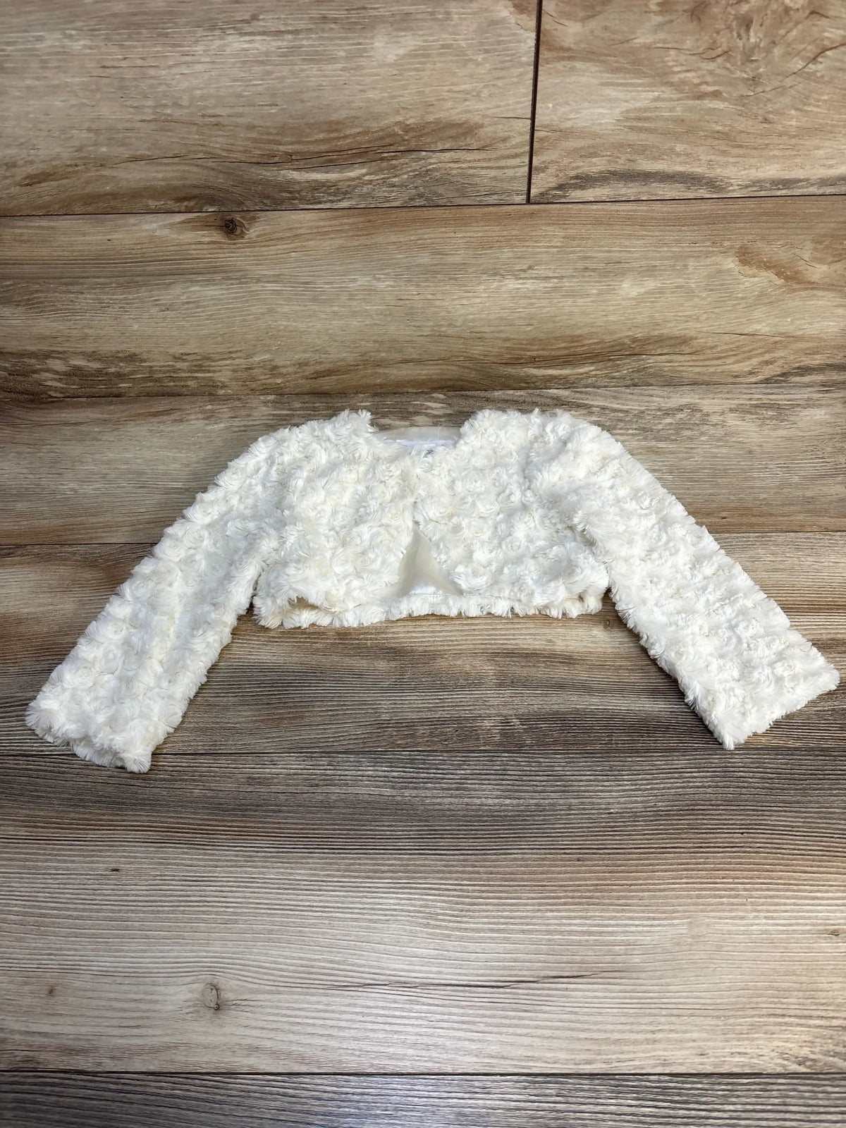 Flat lay of Bonnie Jean Rosette Print Cardigan in white showcasing textured rosette fabric and cropped long sleeves on wood plank floor