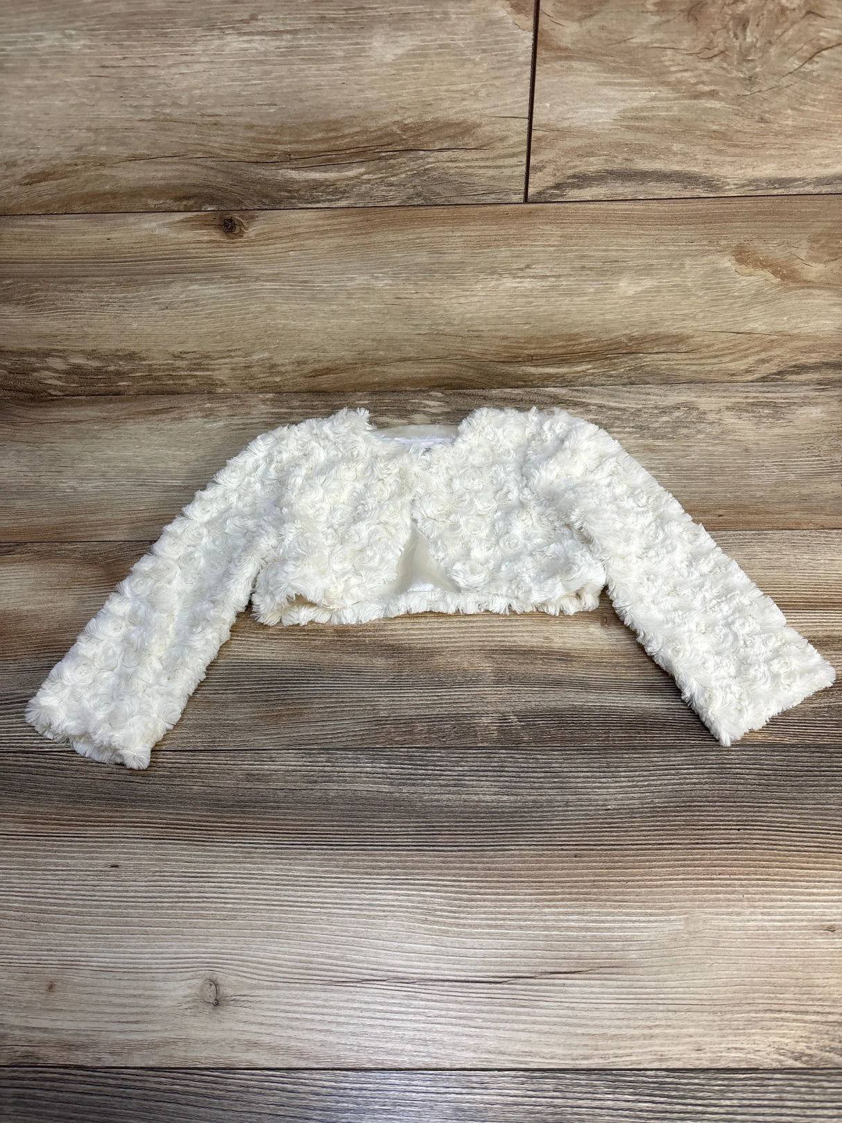 Flat lay of Bonnie Jean Rosette Print Cardigan in white showcasing textured rosette fabric and cropped long sleeves on wood plank floor