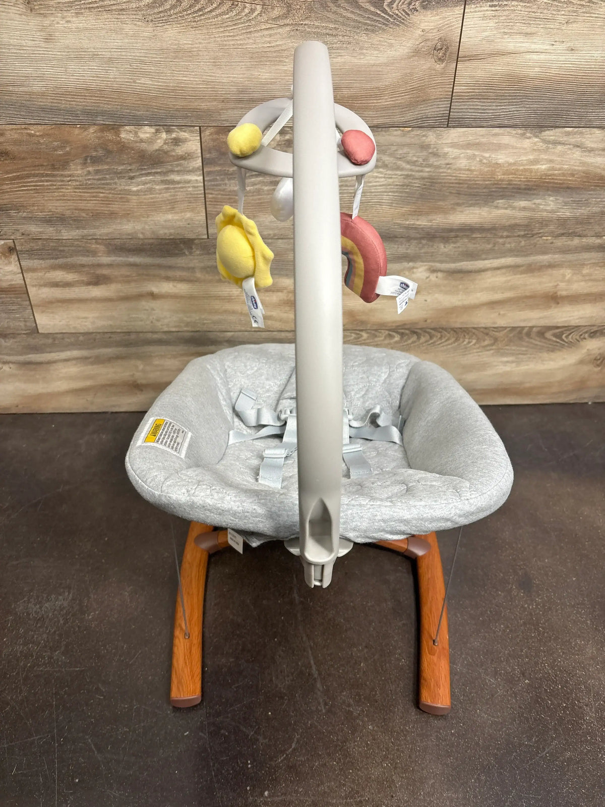 Front view of Chicco Float baby seat in Cloud with gray padded seat, safety harness and detachable toy bar against wood wall