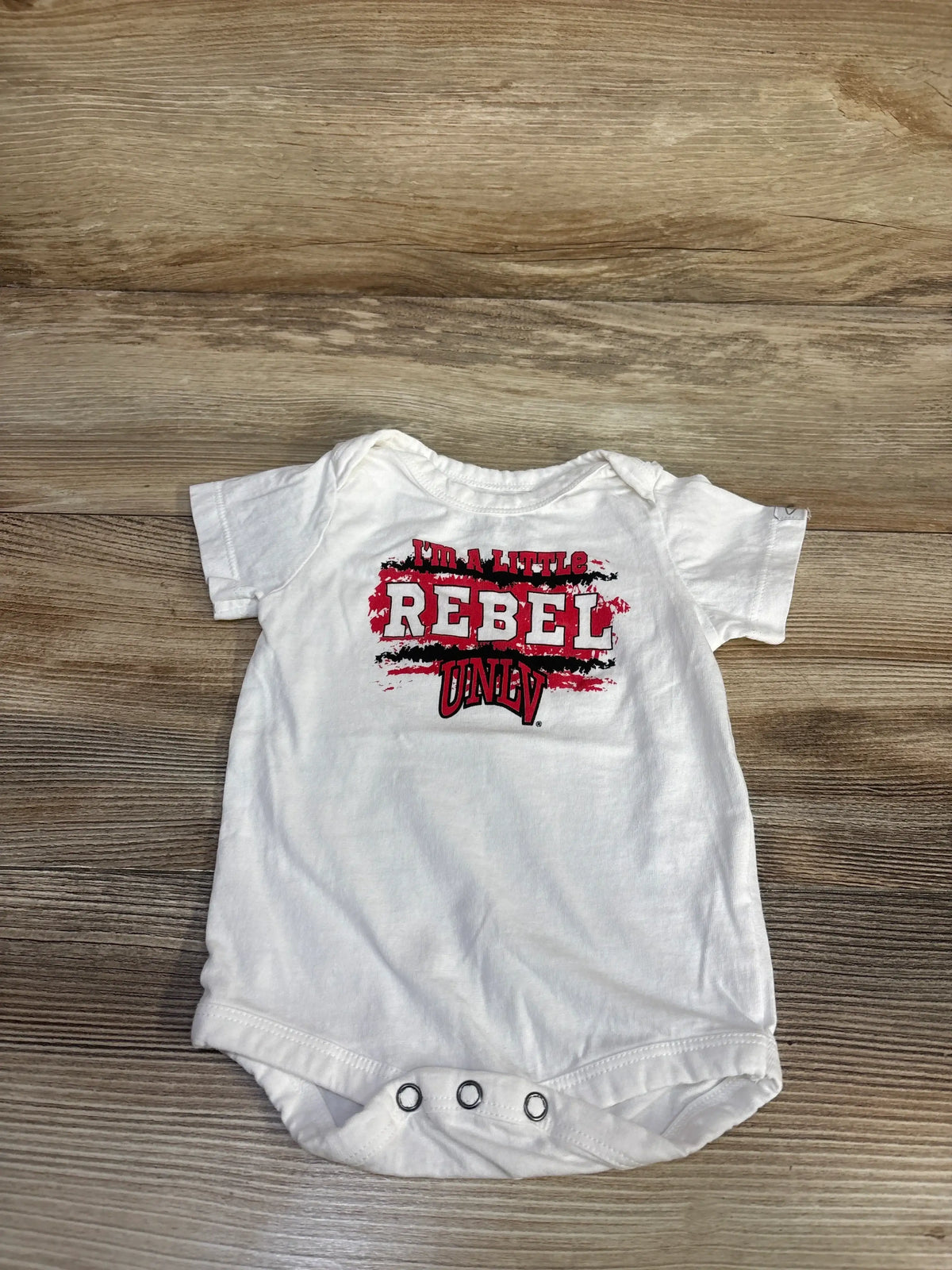 Front view of Garb I’m A Little Rebel UNLV bodysuit in white, showcasing short sleeves, chest graphic, and three snaps on wood