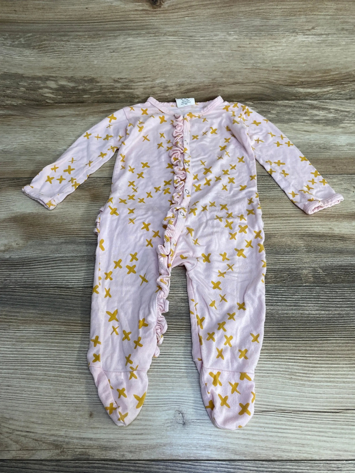 Flat lay of pink Spearmint Love zip footie size 6-9 months showing center ruffle trim and yellow cross print on light wood background