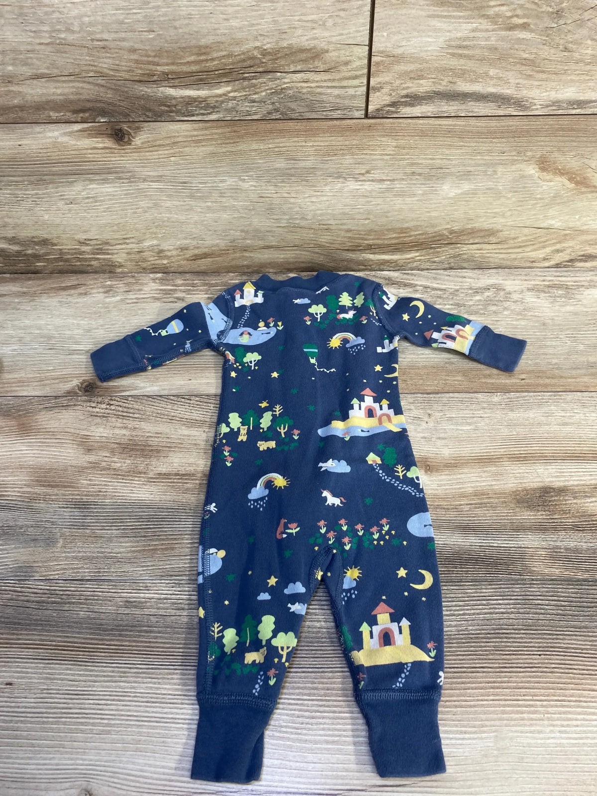 Flat lay of newborn blue Hanna Andersson sleeper showcasing all-over castle and nature print, long sleeves and cuffed ankles on wood background