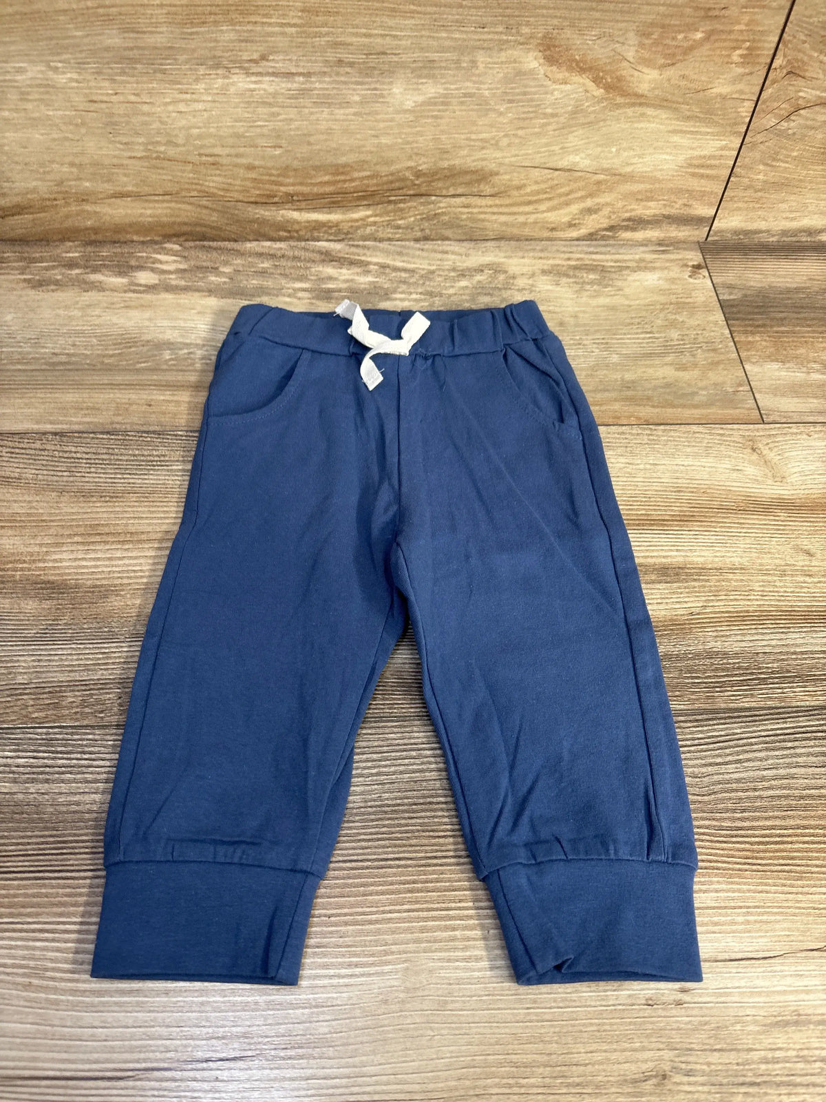 Front view of blue drawstring pants for toddlers, size 18 to 24 months, showcasing drawstring waist and pockets on a wood floor