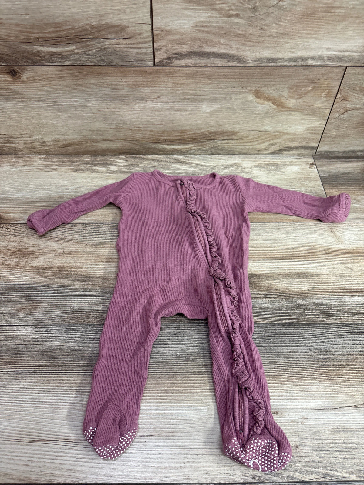 Front view of pink bamboo knit ruffle zipper footie showcasing its ruffled zipper and covered feet on wood flooring