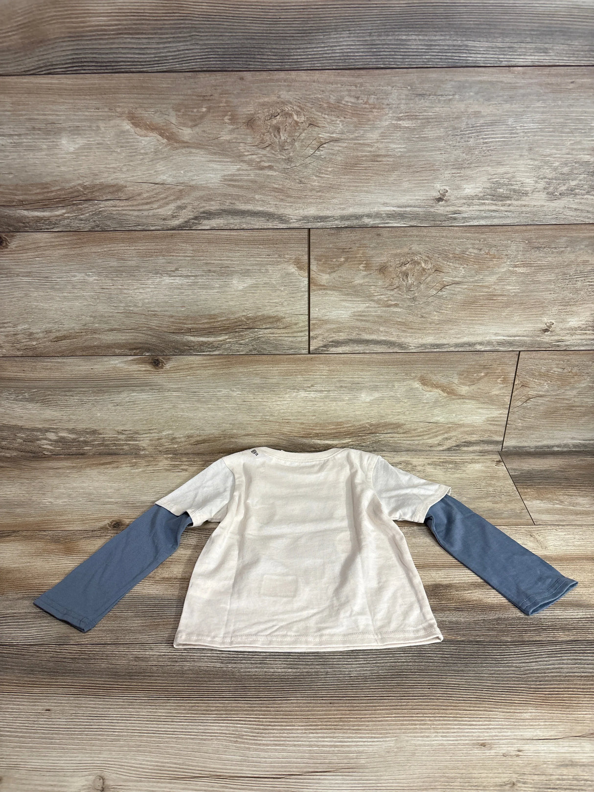 Back view of Children’s Place Rescue Patrol long-sleeve toddler shirt size 2T showing beige body with blue attached long sleeves laid flat on wood background