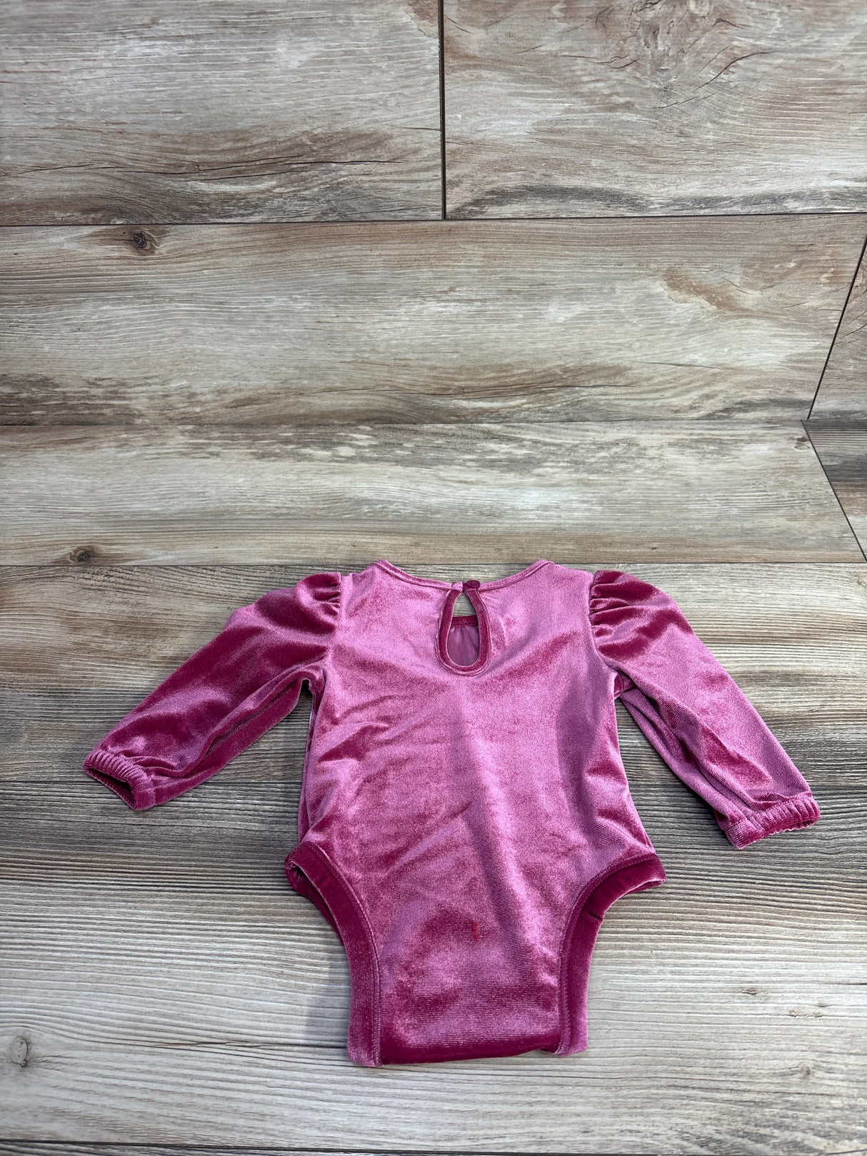 Pink velvet long sleeve baby bodysuit on wood background, gently used kids clothing