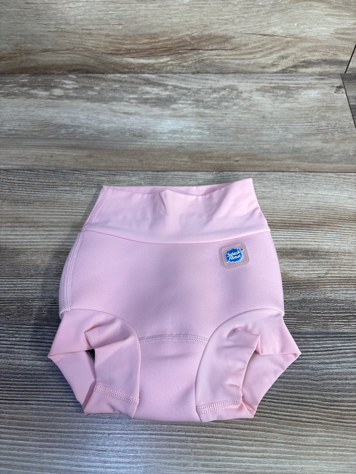 Top-down view of pink Splash About Happy Nappy swim diaper showcasing high-rise waistband and snug leg cuffs on wood background