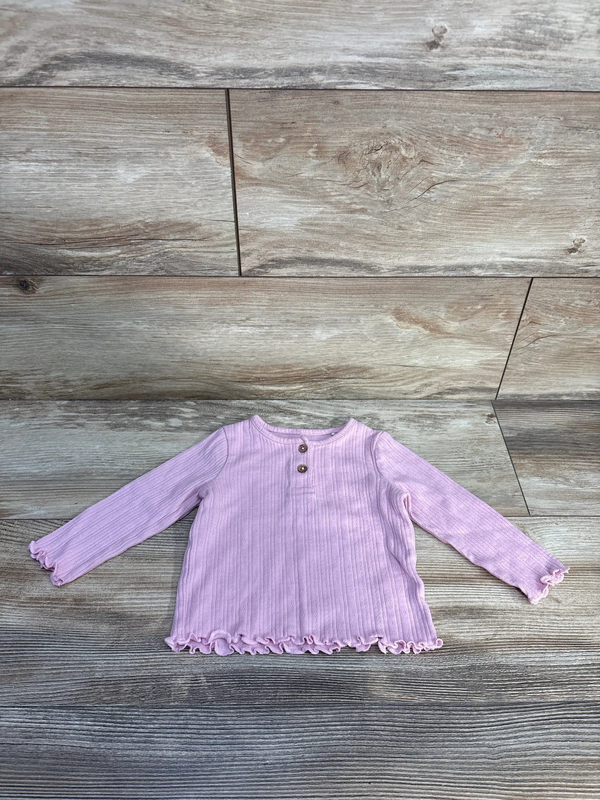 Front view of Topomini pink ribbed henley shirt, size 3-6 months, with two-button neckline and ruffled trim on wood surface