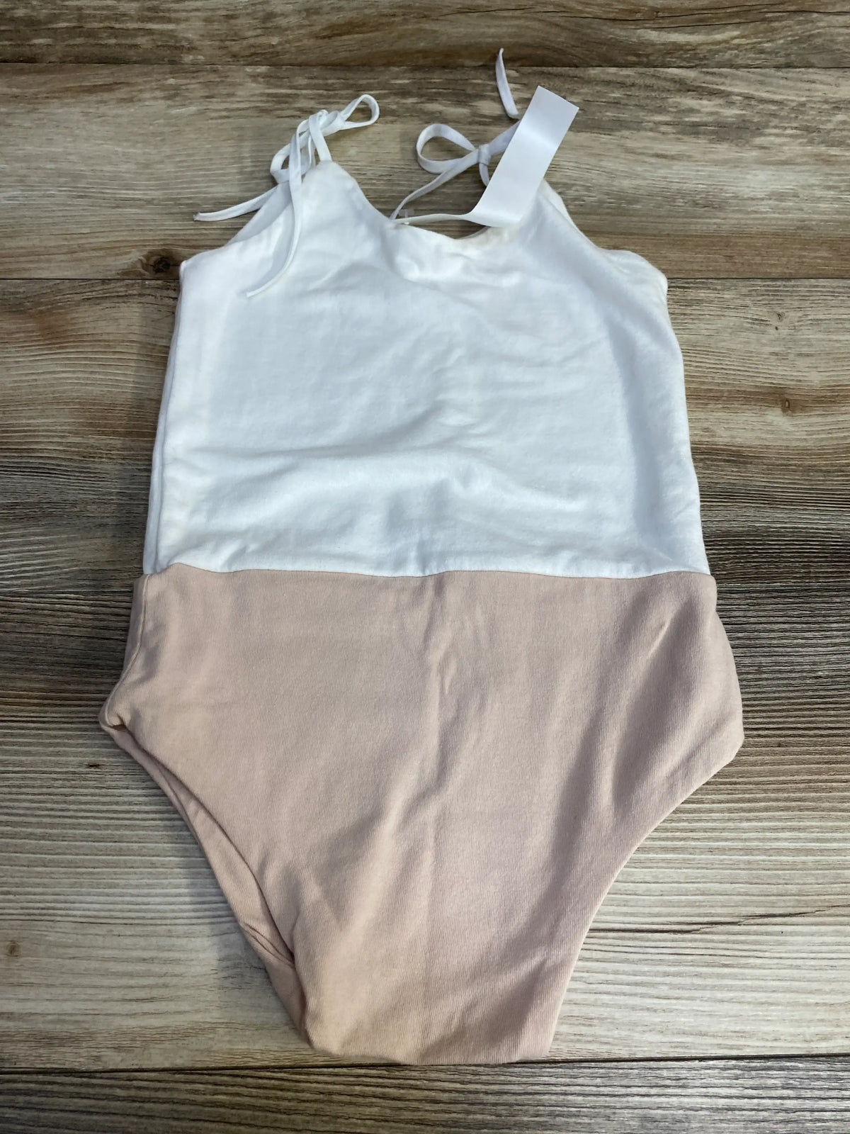 Flat lay of Wraredoll toddler leotard size 4-5T showing white top, light pink bottom, and tie shoulder straps on wood-grain background