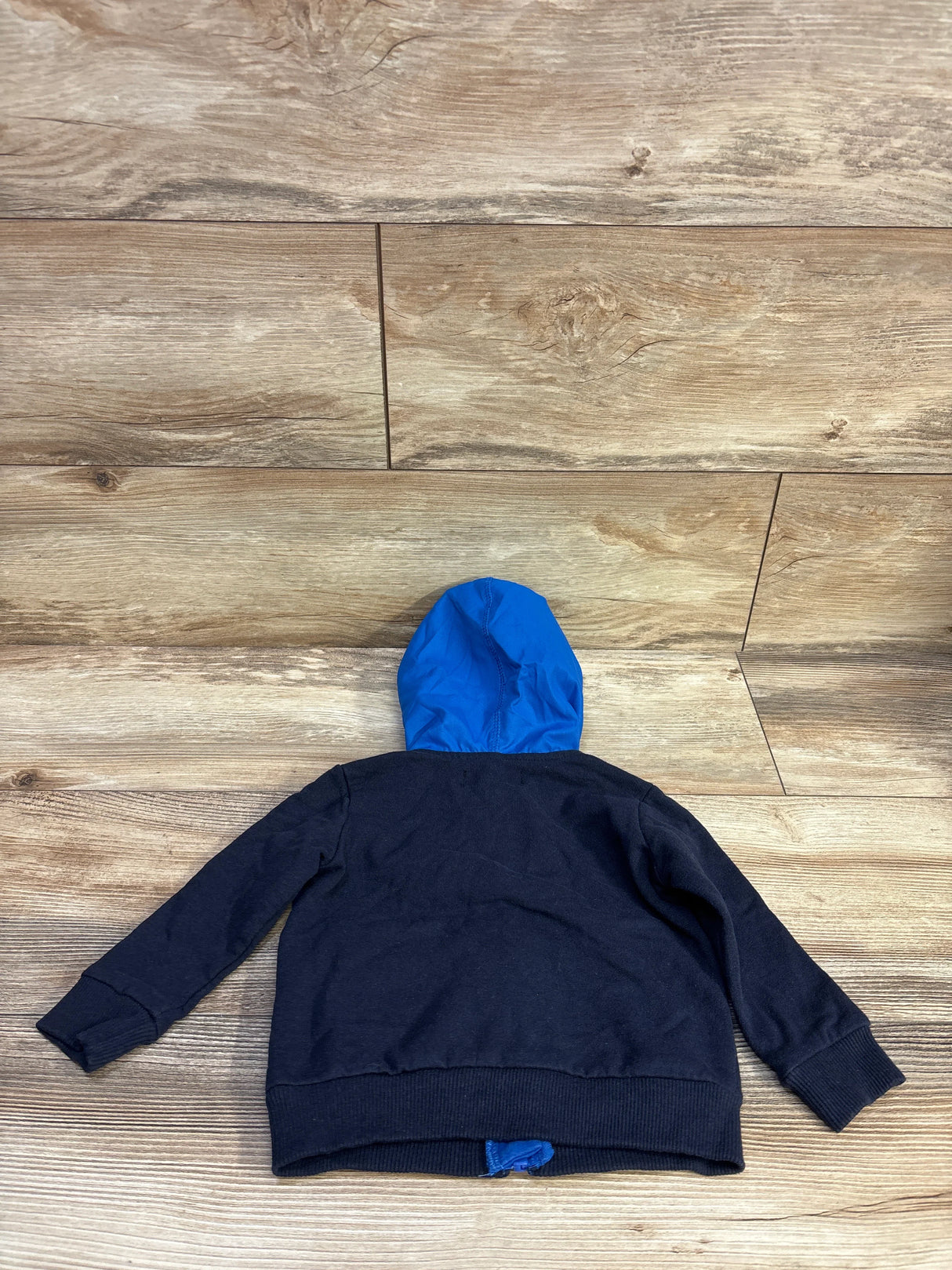 Back view of navy toddler waterproof full-zip jacket size 12M showcasing bright blue hood on wood floor