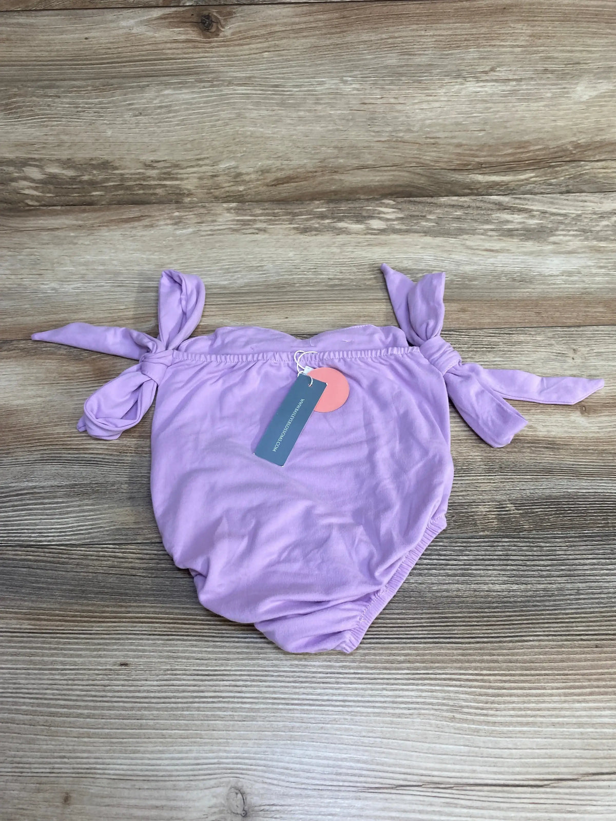 Flat lay of purple toddler sleeveless leotard size 2T showing knotted shoulder ties and retail hang tag on wood background