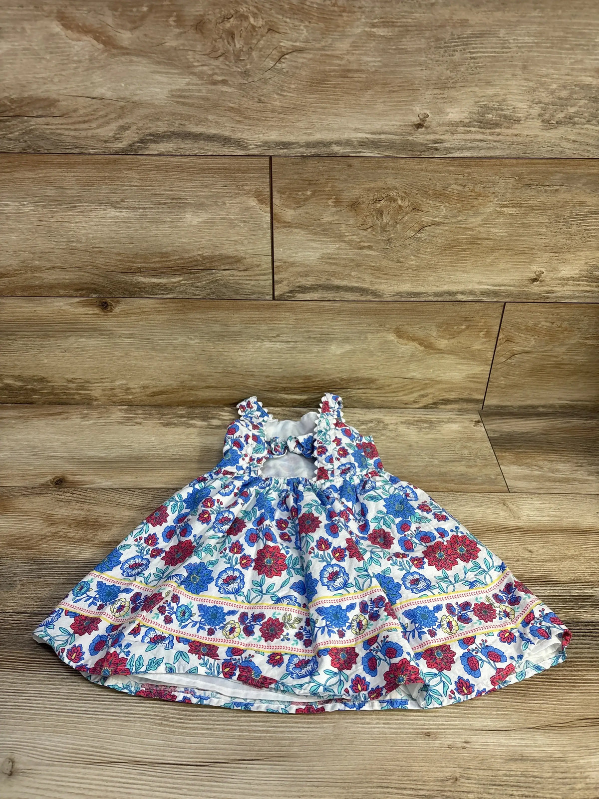 Front view of girls' Btween floral sleeveless dress size 2T with ruffled straps and gathered skirt on wood background