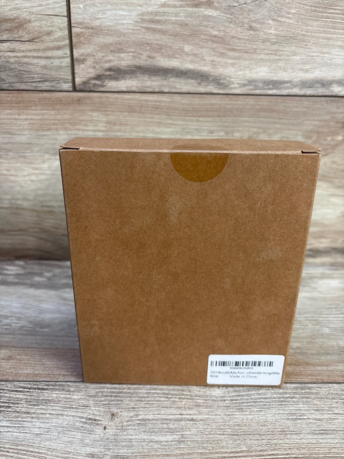 Back view of Sili Factory reusable baby food pouch set packaging with a small label on a wood-grain background