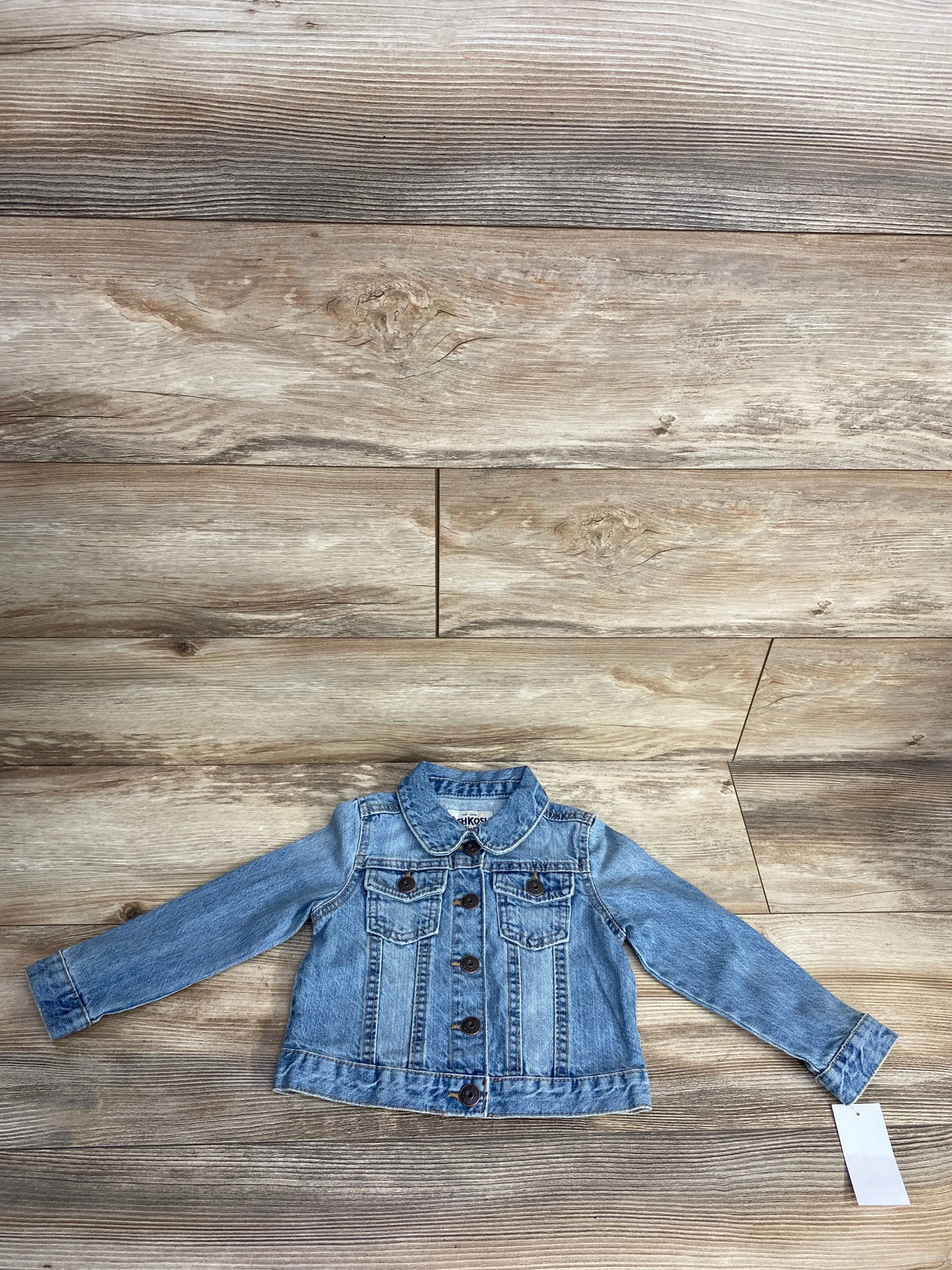 Light blue denim jacket for kids with button front and flap chest pockets on wood background