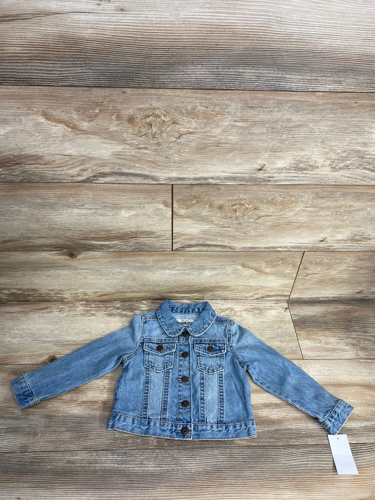 Light blue denim jacket for kids with button front and flap chest pockets on wood background