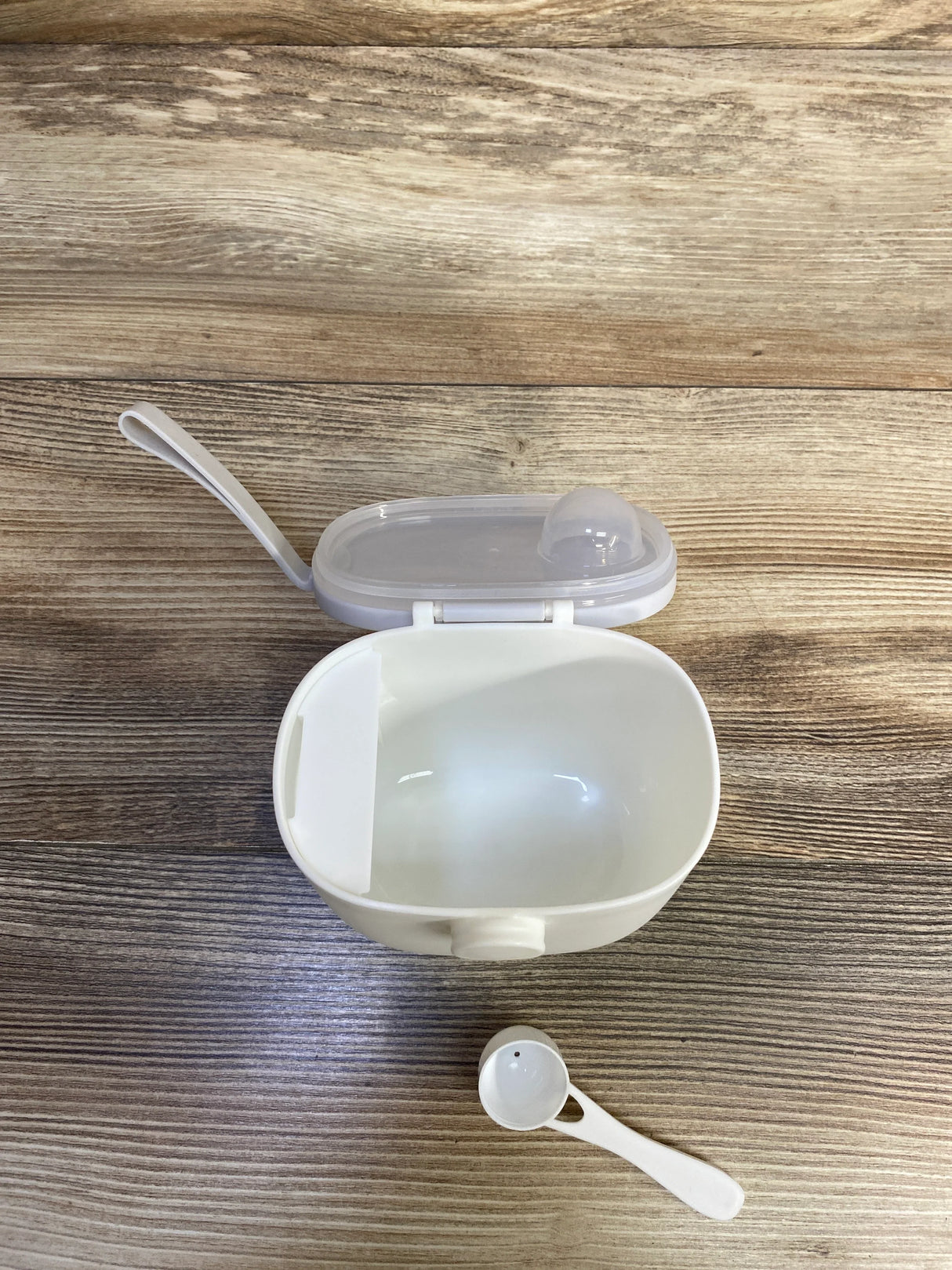 Top-down view of Termichy baby formula dispenser with open lid, removable scoop, and inner divided compartment on wood background