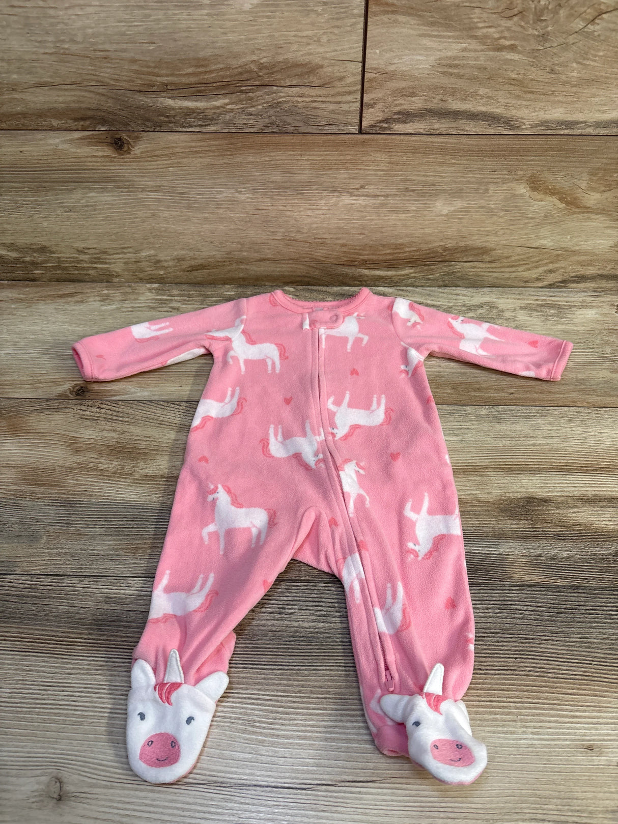 Flat lay of Child Of Mine pink blanket sleeper showing white unicorn print and plush unicorn footies on wood floor