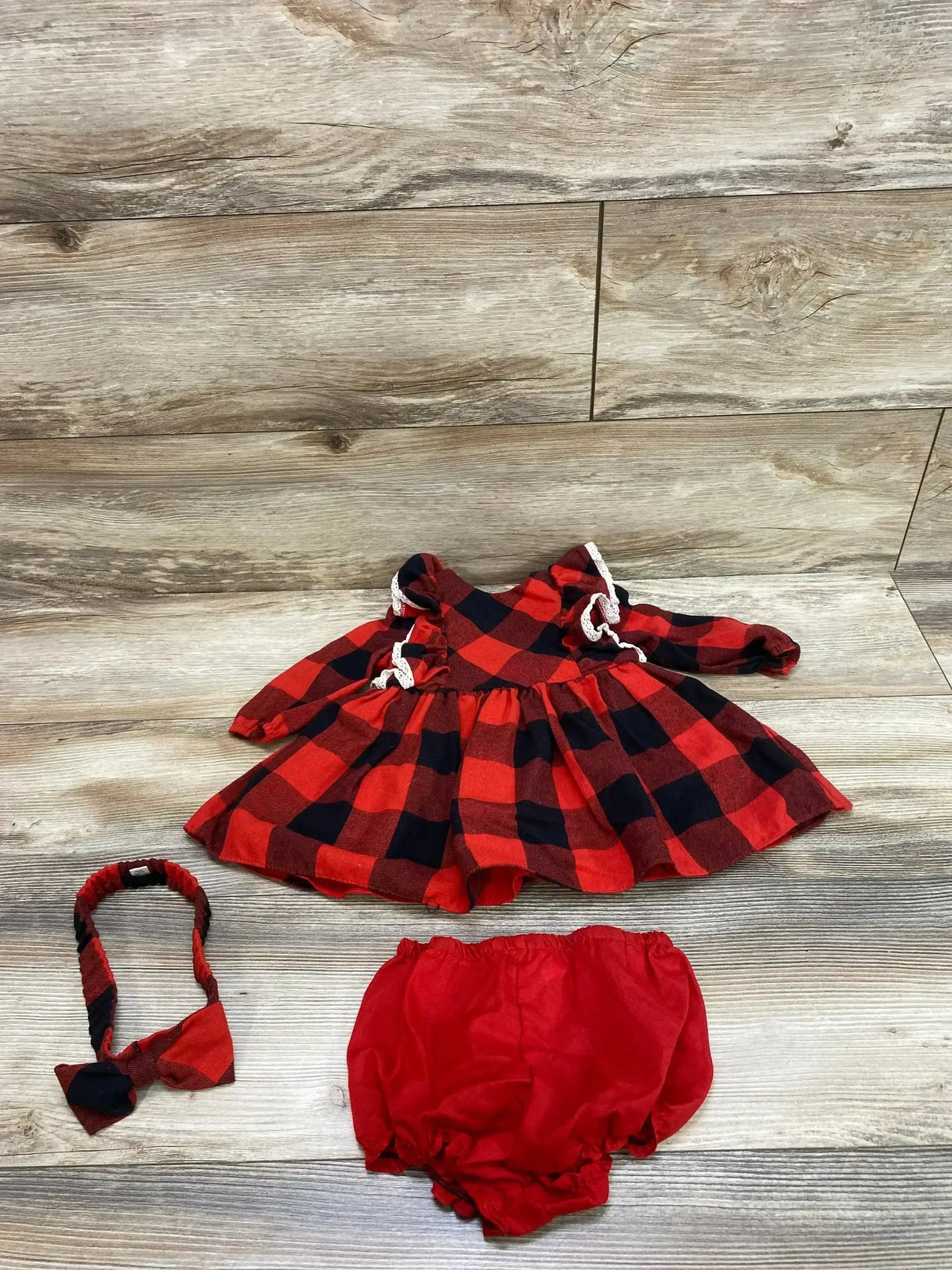 Flat lay of red and black buffalo-check long-sleeve dress with lace trim, matching bloomers and headband on wood background