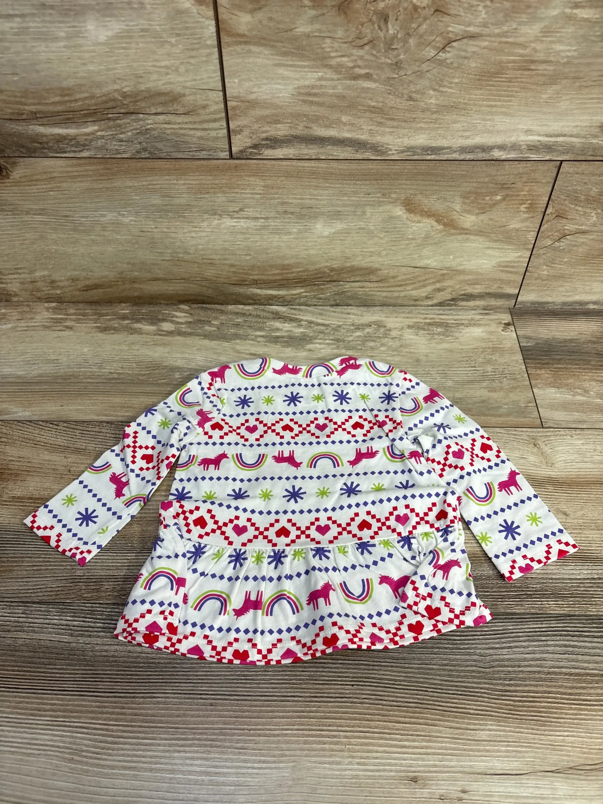 Children's long-sleeve white shirt with colorful unicorn, rainbow, and heart patterns on wooden floor